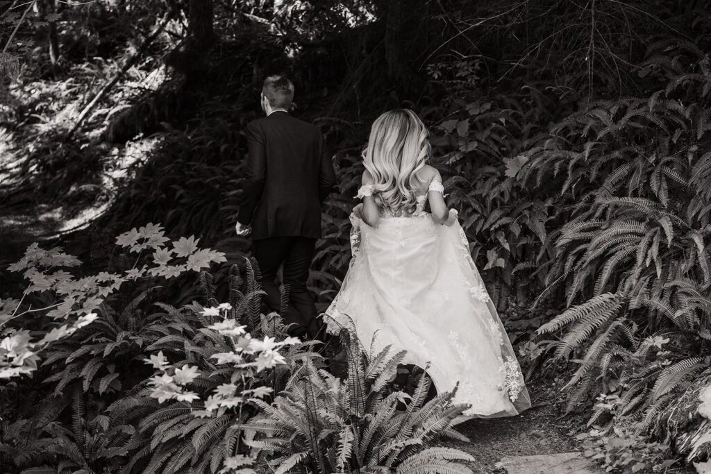 Bride and groom walk down a forest trail during their Mount Rainier elopement 