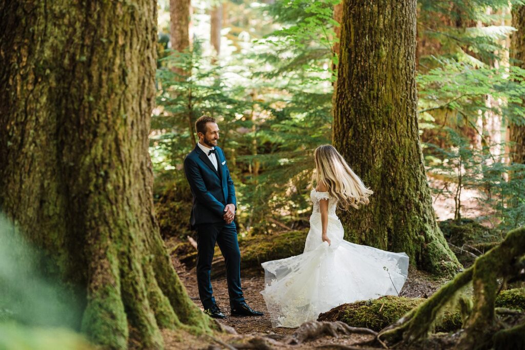 Bride dances in the forest while groom watches and smiles 