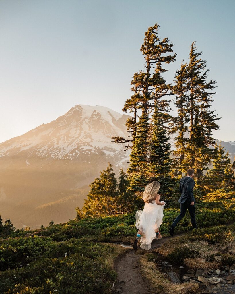 Bride and groom run through a mountain trail during their elopement at Mt Rainier National Park