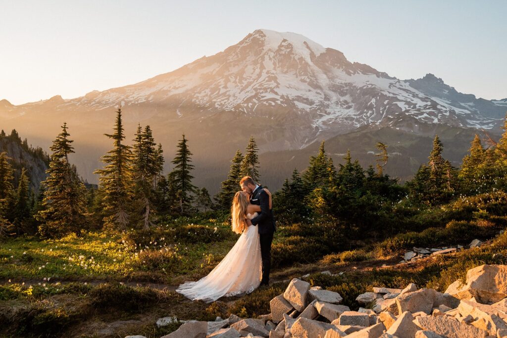 Bride and groom kiss on a mountain trail at sunset in front of Mount Rainier 