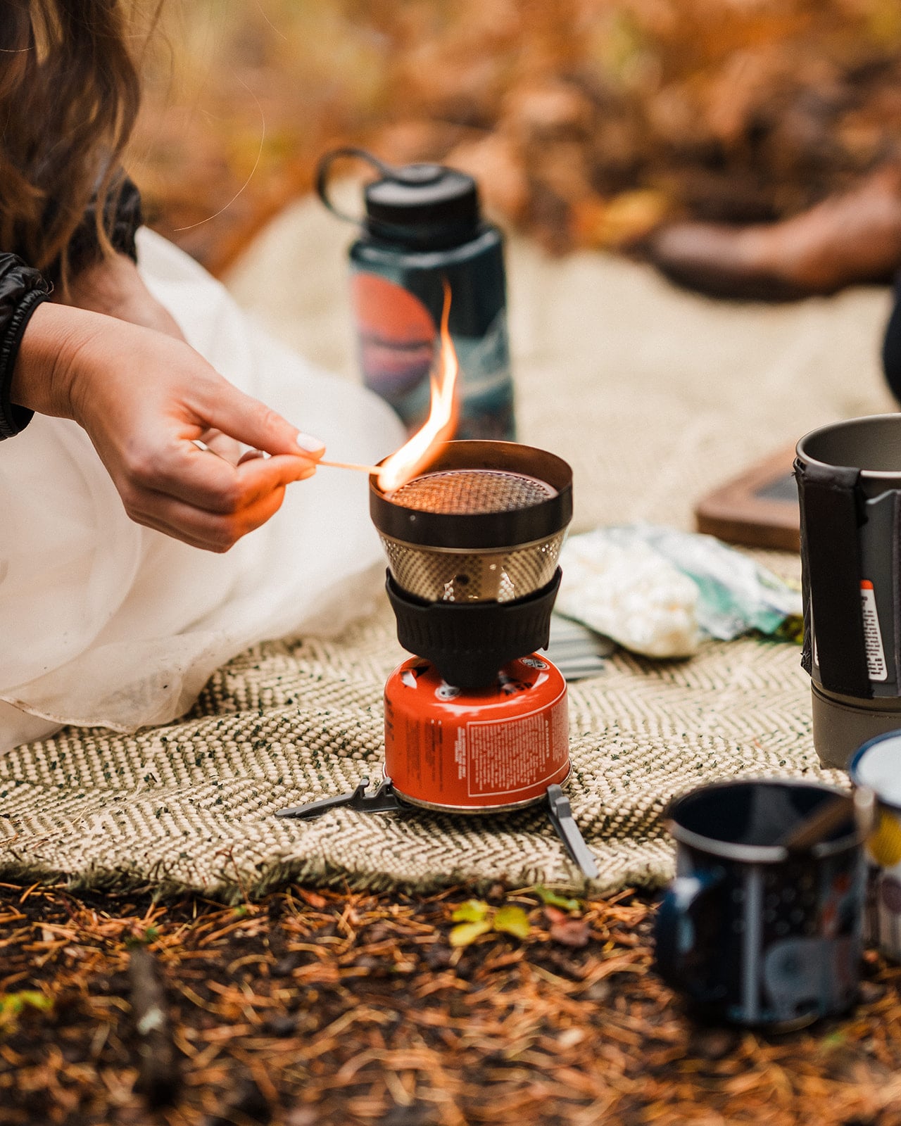 Bride lights a camp stove to make hot chocolate during their fall wedding picnic