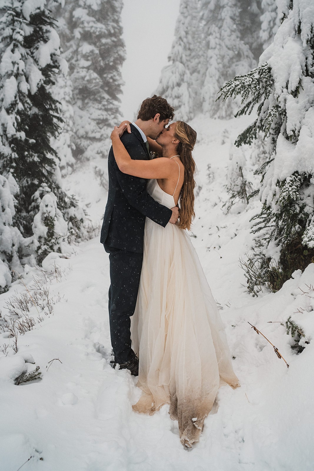 Bride and groom kiss on a snowy trail in Mt Rainier National Park at the end of their fall wedding in Washington