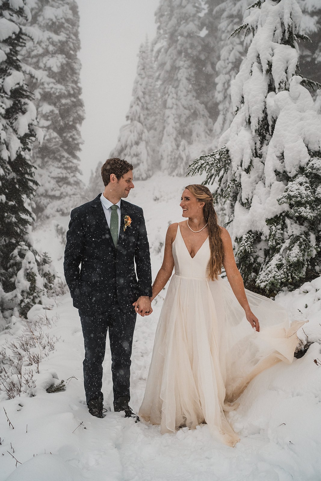 Bride and groom hold hands on a snowy trail in Mt Rainier National Park at the end of their fall wedding in Washington