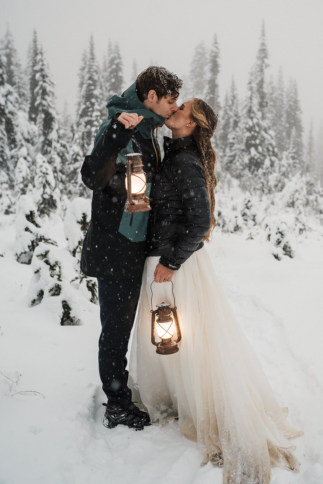 Bride and groom kiss while holding lanterns on a snowy trail in Mt Rainier National Park at the end of their fall wedding in Washington