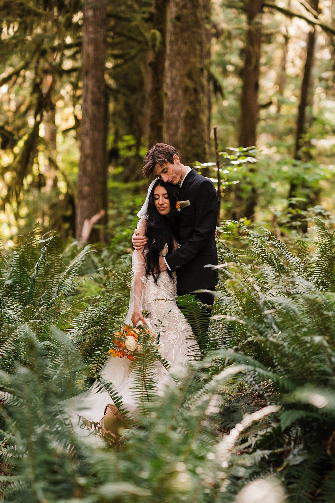 Bride and groom hug one a fern-filled forest trail at their elopement in Mt Baker