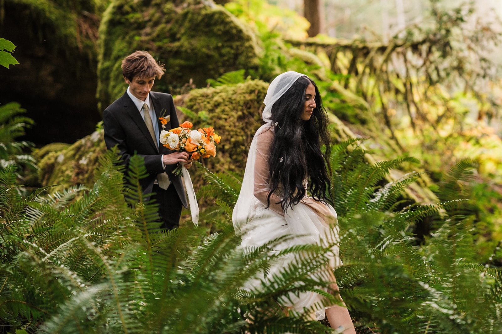 Bride and groom walk through a fern-filled forest trail at their Mt Baker elopement