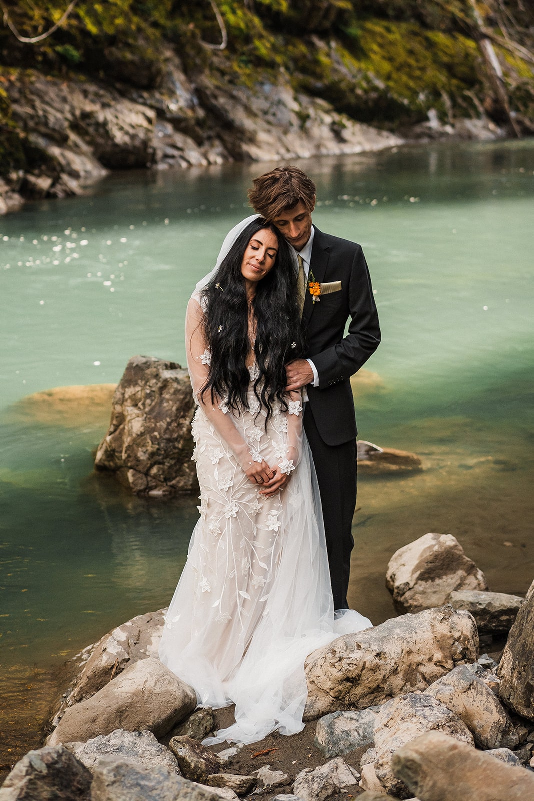 Bride and groom lean their heads against each other while standing by a river during their Mt Baker elopement 