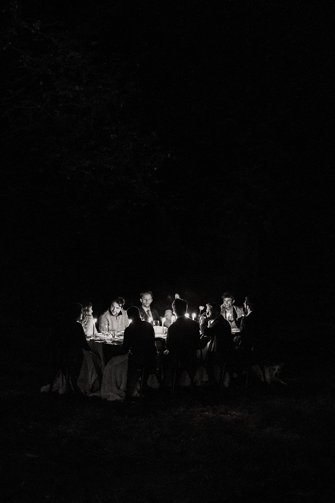 Bride and groom enjoy dinner with their guests at an Airbnb candlelit reception in the forest 