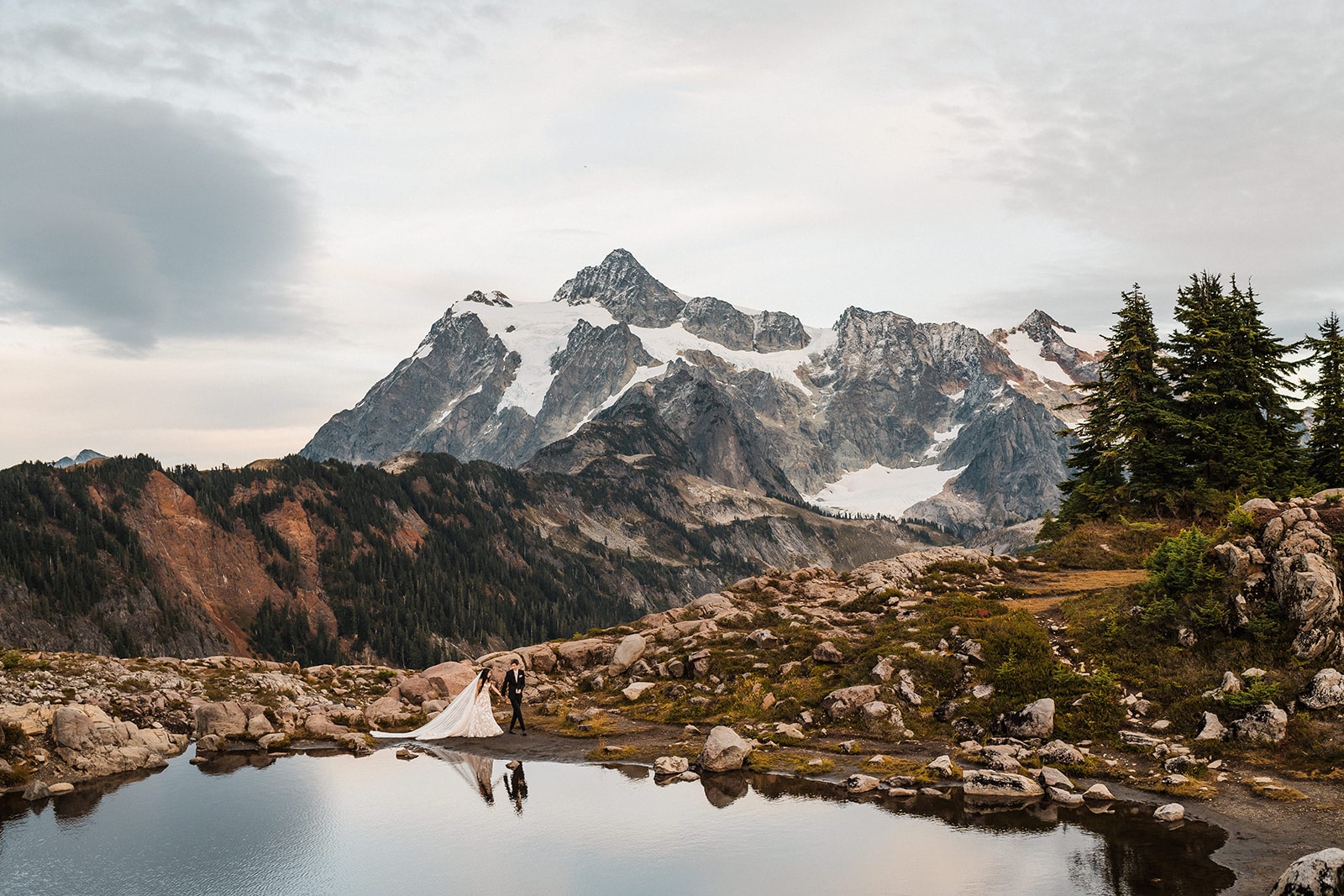 Bride and groom hold hands while walking around an alpine lake during their adventure elopemetn at Artist Point