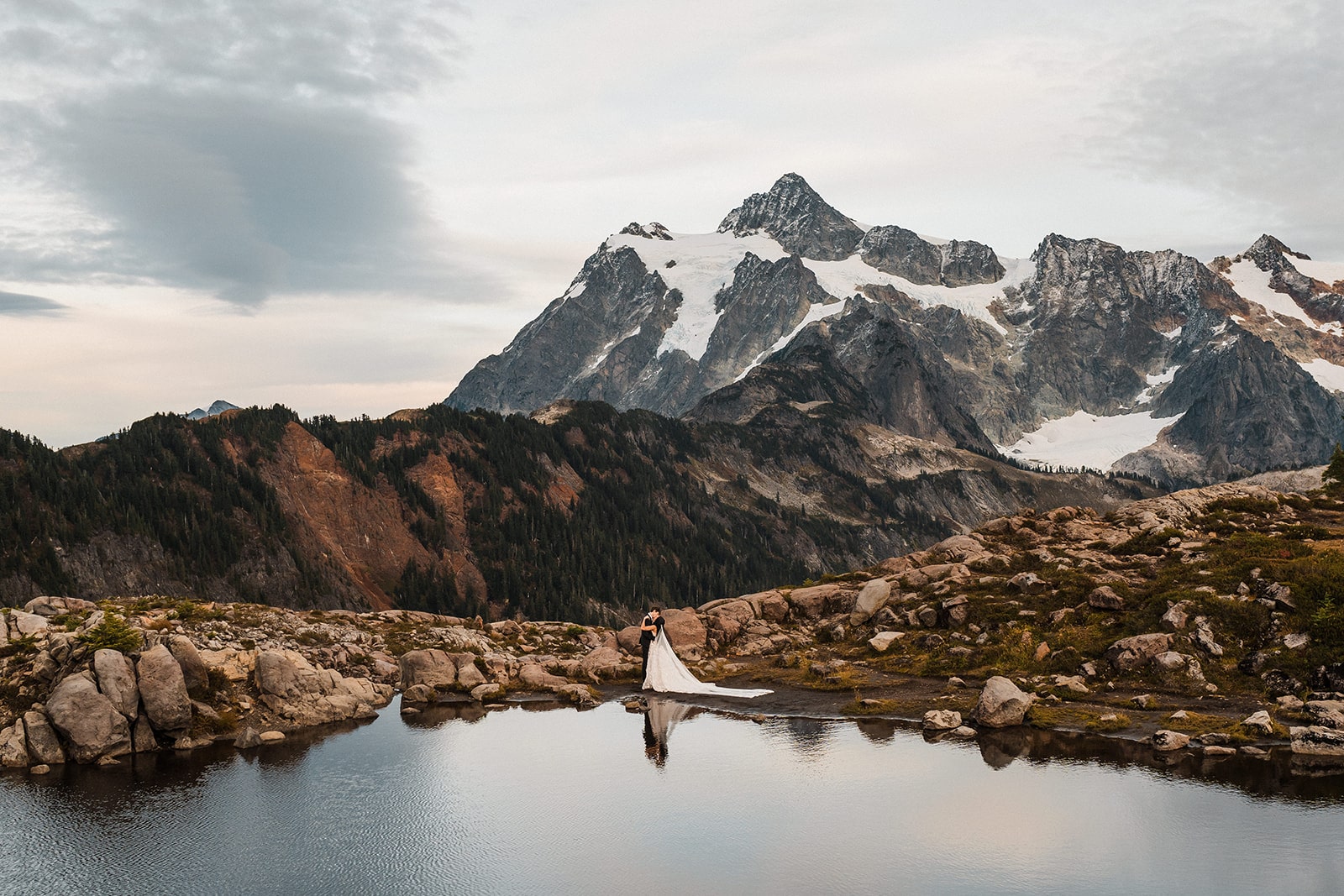 Bride and groom kiss by an alpine lake in front of a mountain at Artist Point