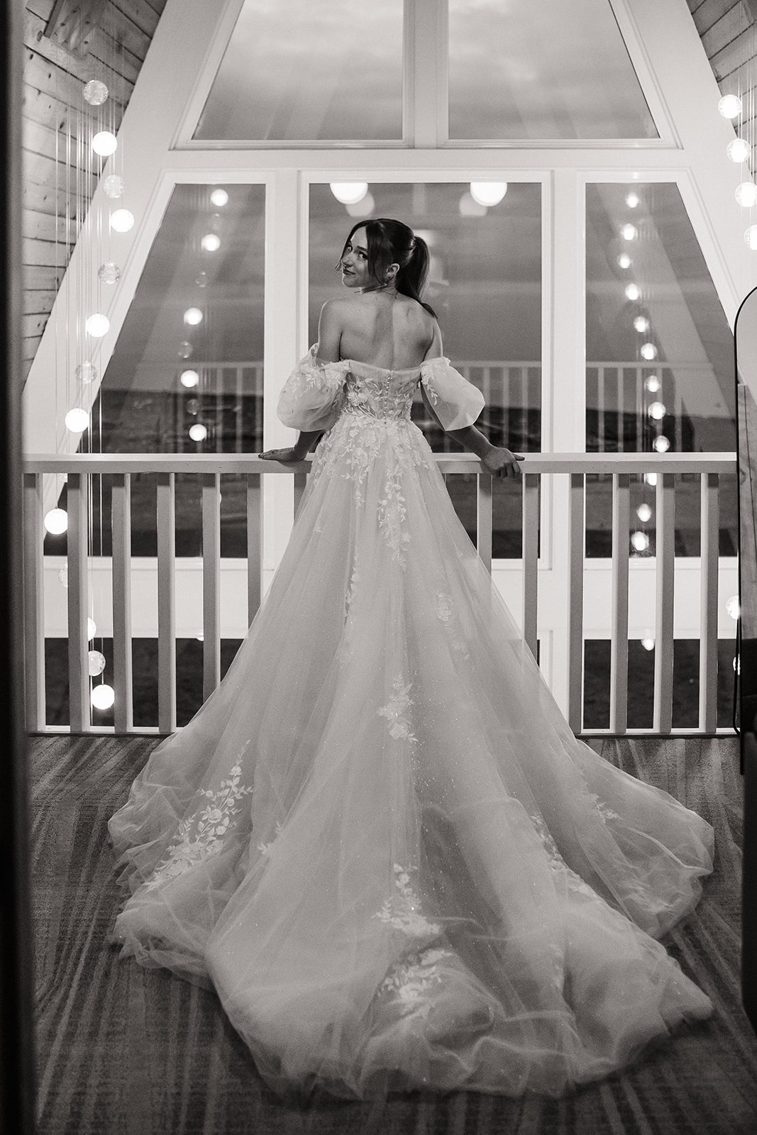 Bride rests across a railing at Agate Beach Lodge while her white wedding gown trails behind her