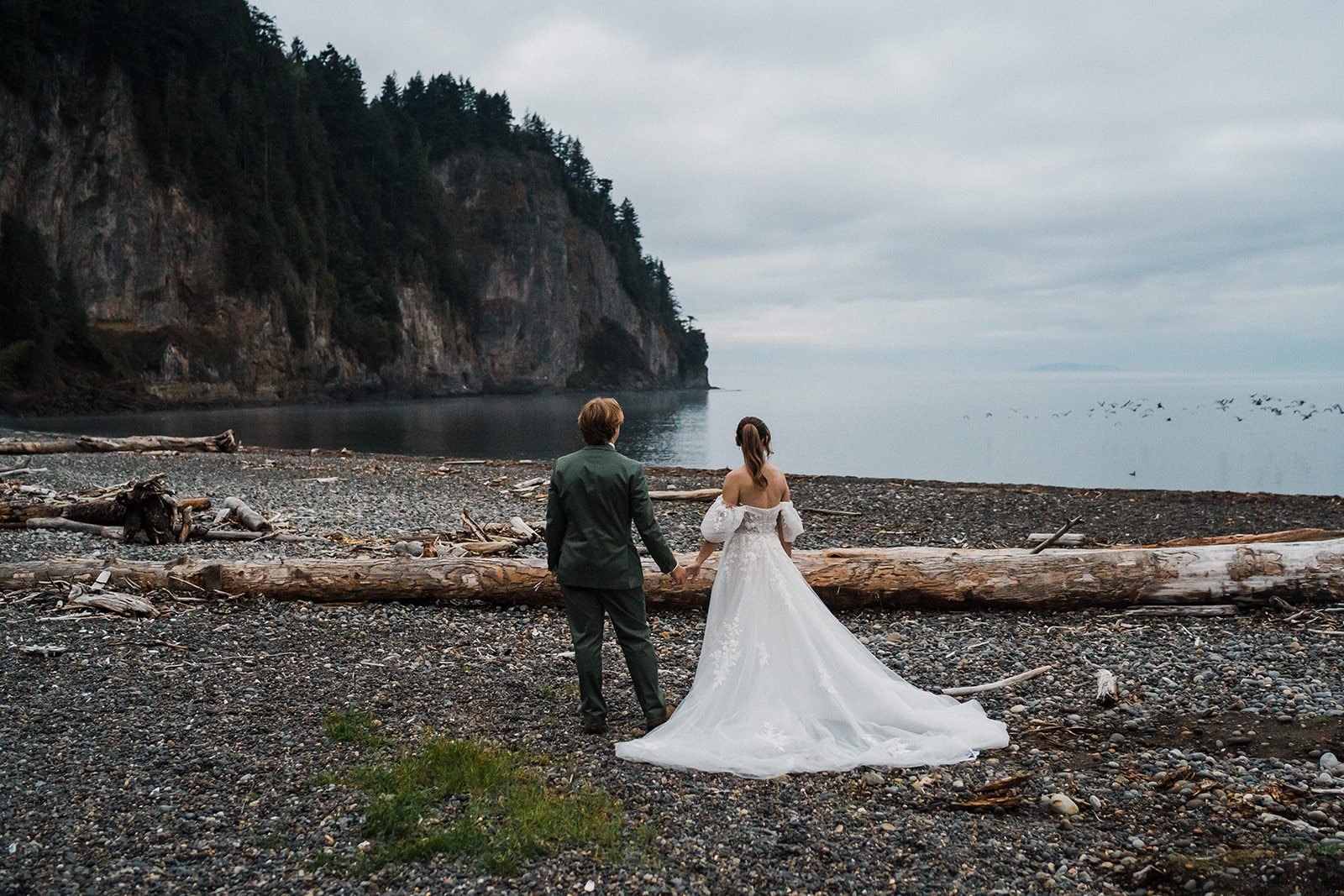 Bride and groom hold hands on a rocky beach at Agate Beach Lodge during their national park elopement on the Olympic Peninsula