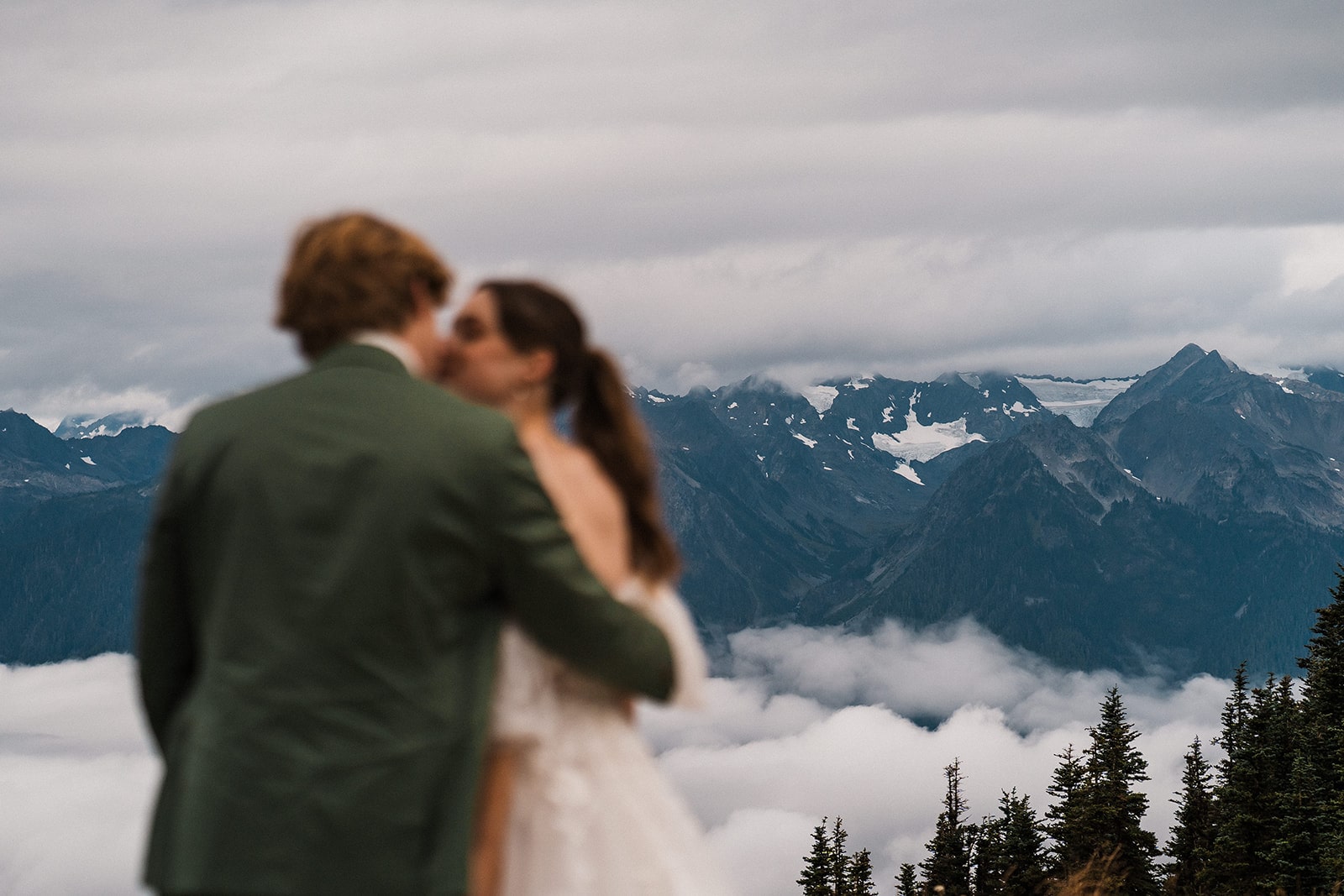 Bride and groom kiss on a trail overlooking foggy mountains at their national park elopement