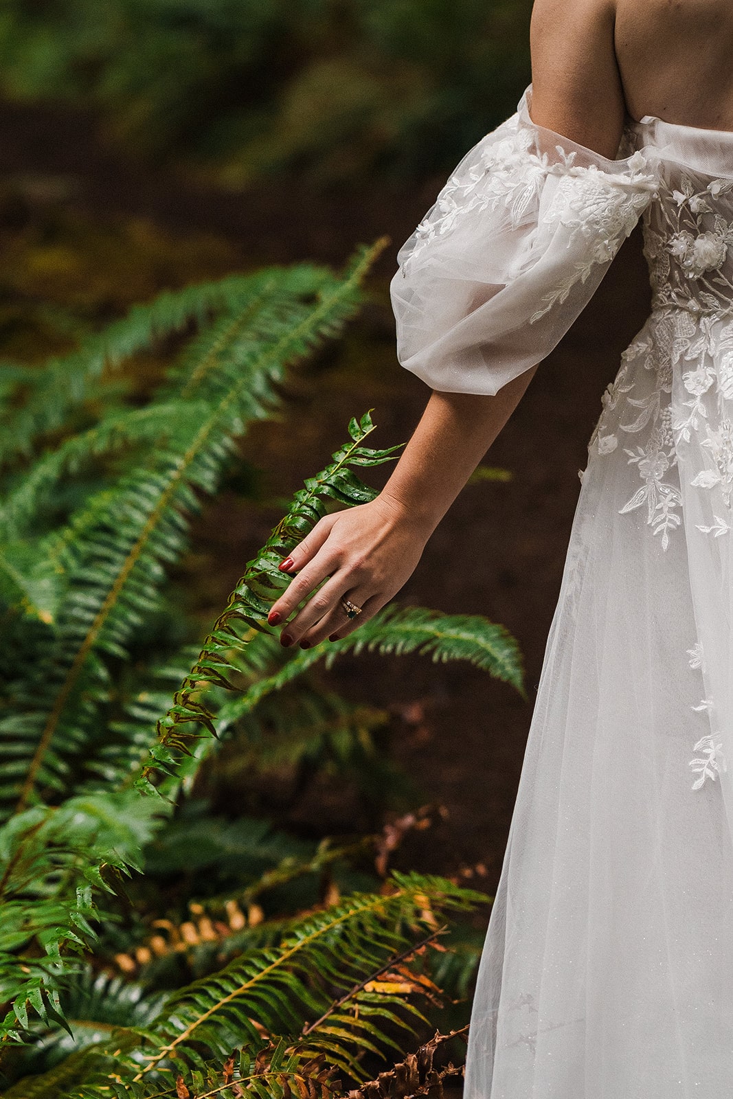 Bride runs her hand along a fern during her forest national park wedding on the Olympic Peninsula