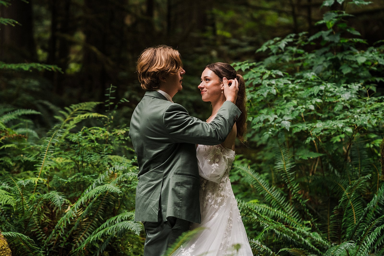 Groom brushes back bride's hair during their forest elopement portraits in Olympic National Park