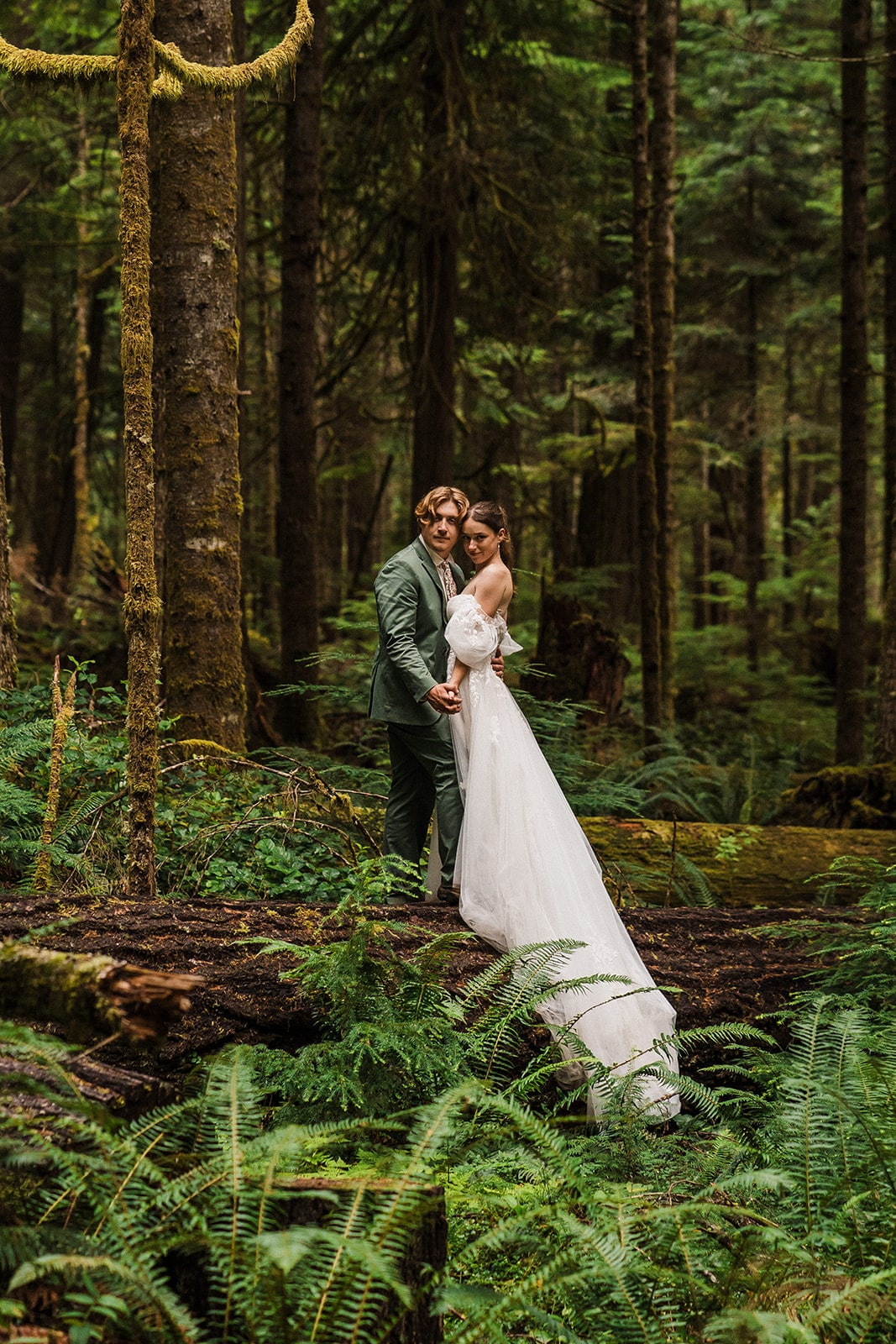 Bride and groom hold hands while standing on a fallen tree during their national park wedding on the Olympic Peninsula