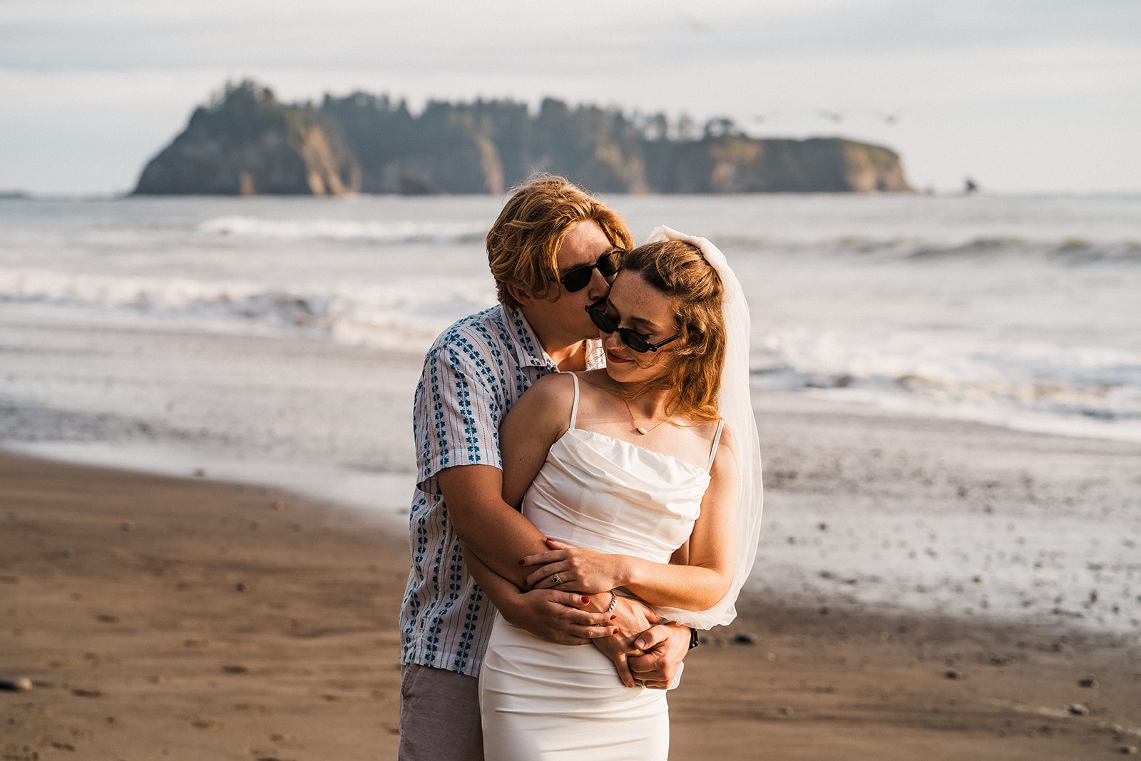 Groom kisses bride behind her ear during their adventure portraits at Rialto Beach