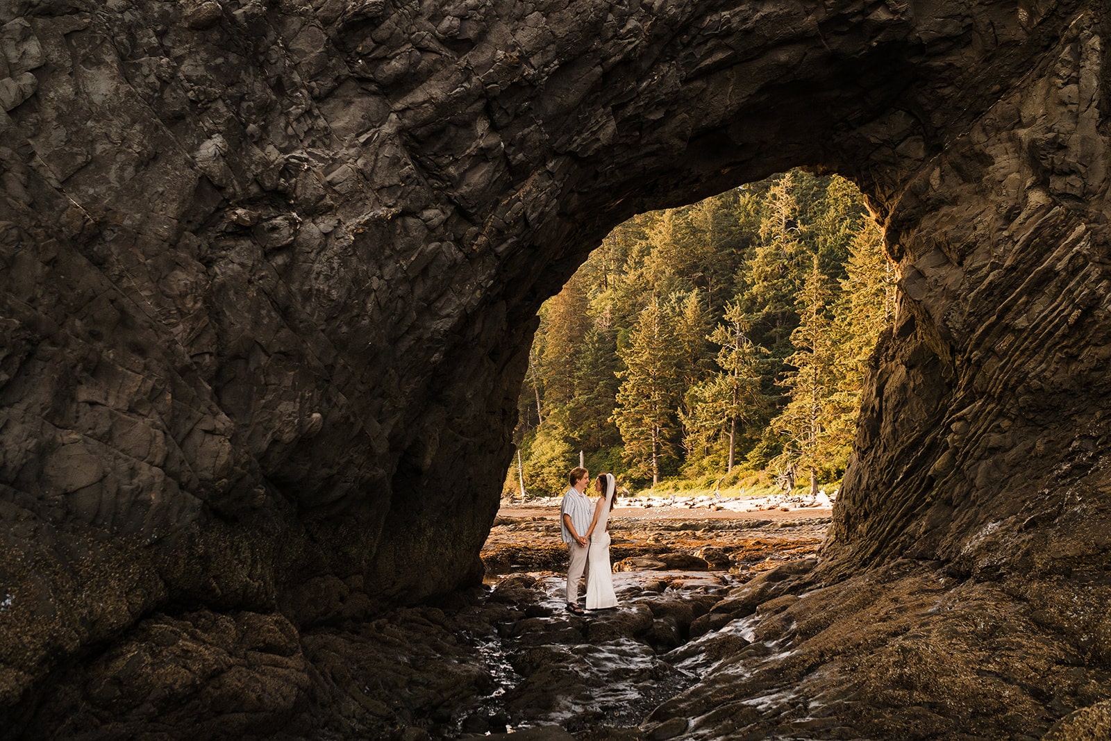 Bride and groom stand under an arch rock at Rialto Beach during their sunset adventure photos