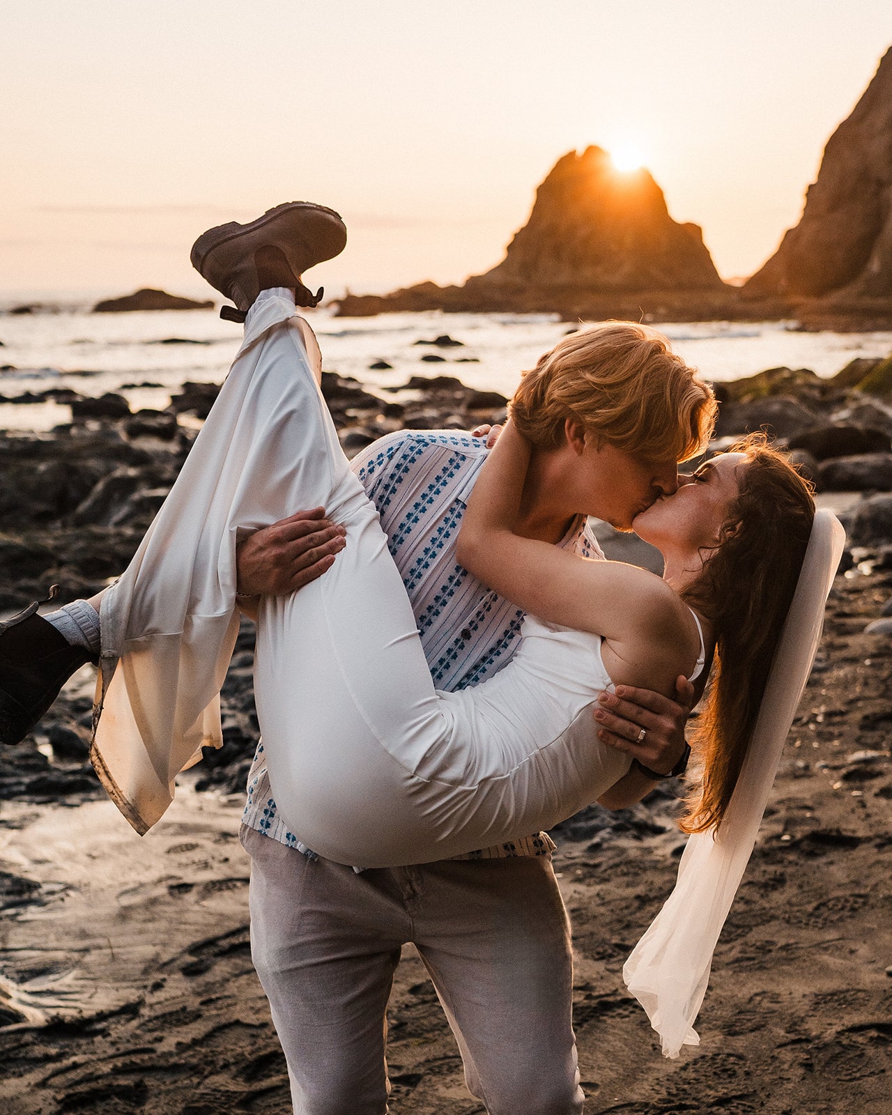 Groom hold bride and dips her back for a kiss on the beach during their sunset adventure photos