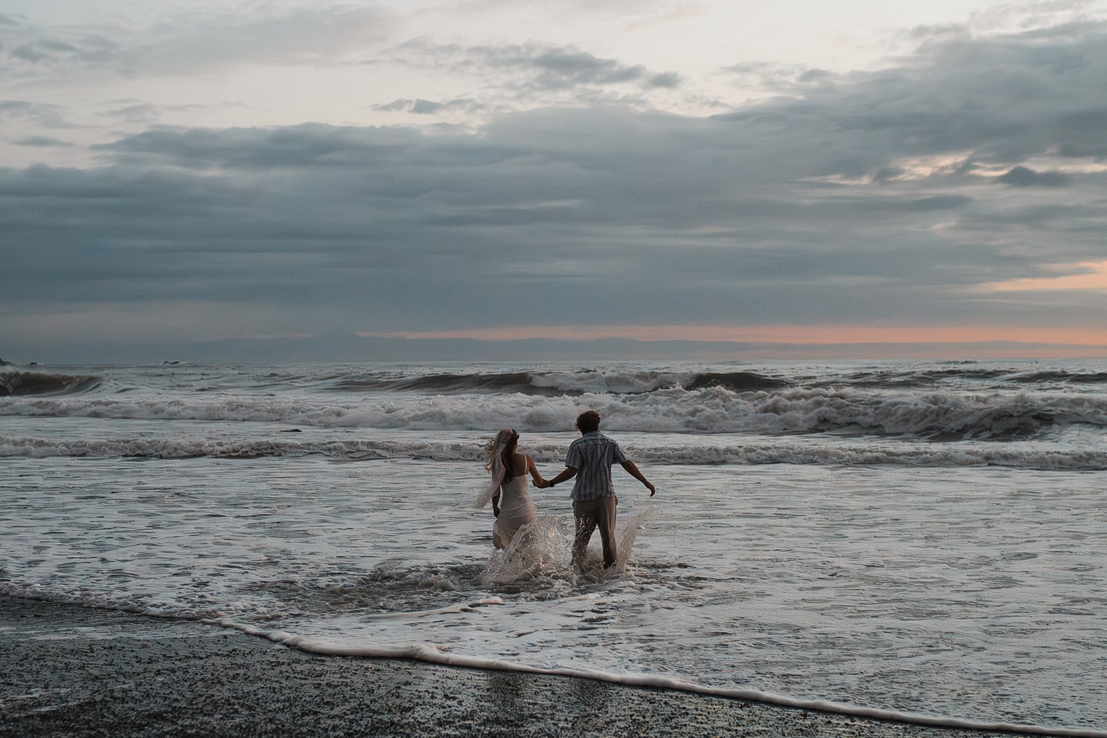 Bride and groom hold hands while running into the ocean at the end of their national park elopement