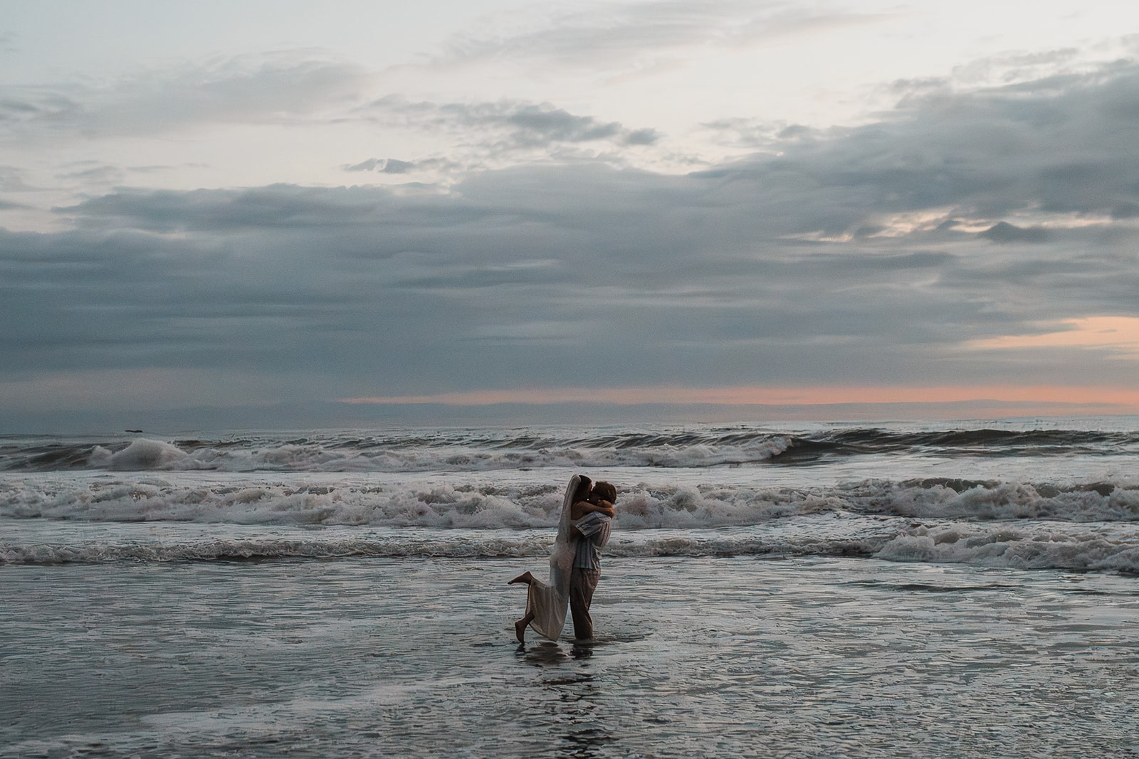 Bride and groom kiss in the ocean at the end of their sunset adventure session on Rialto Beach