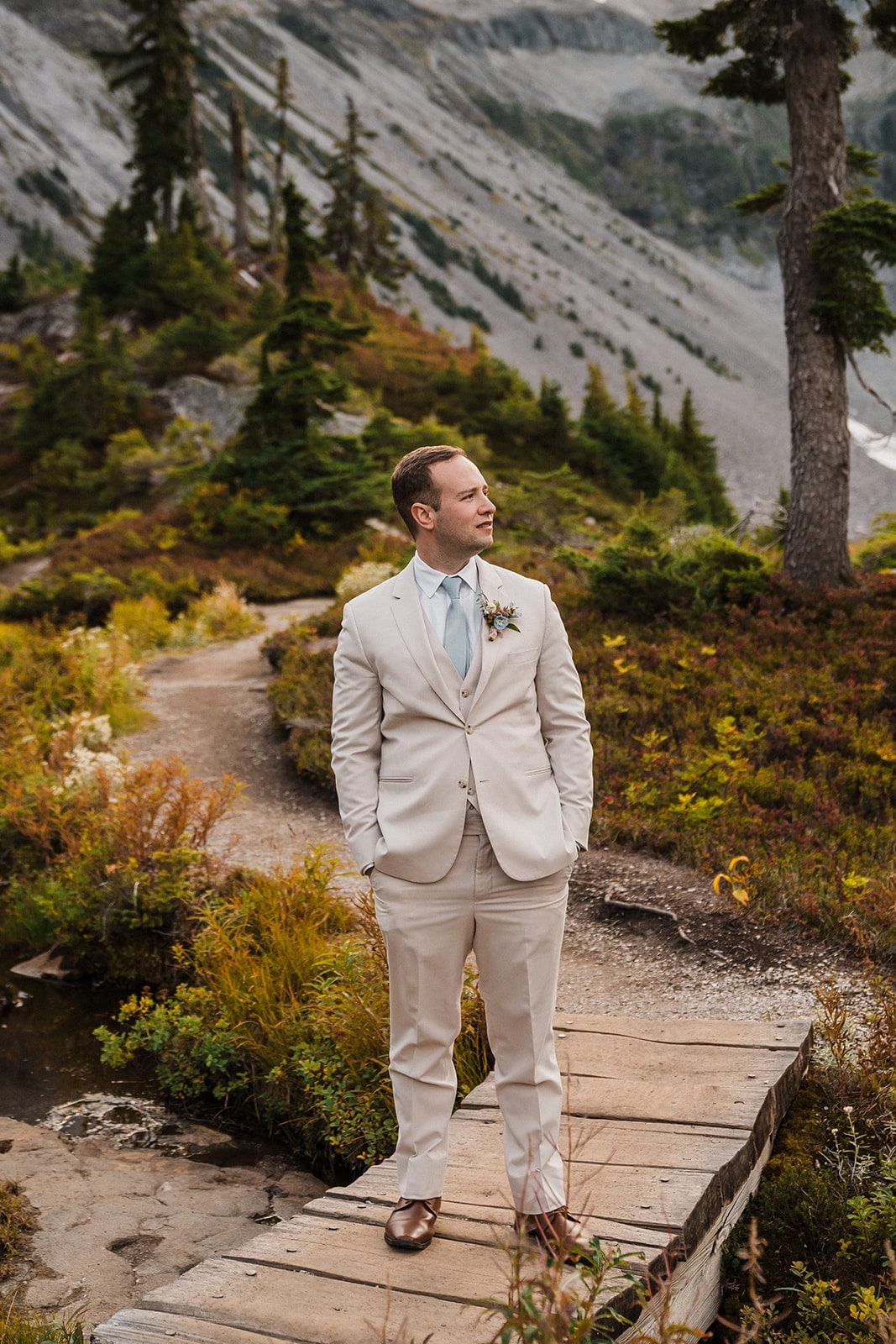 Groom wearing white/beige elopement suit standing on a wood boardwalk during his adventure elopement