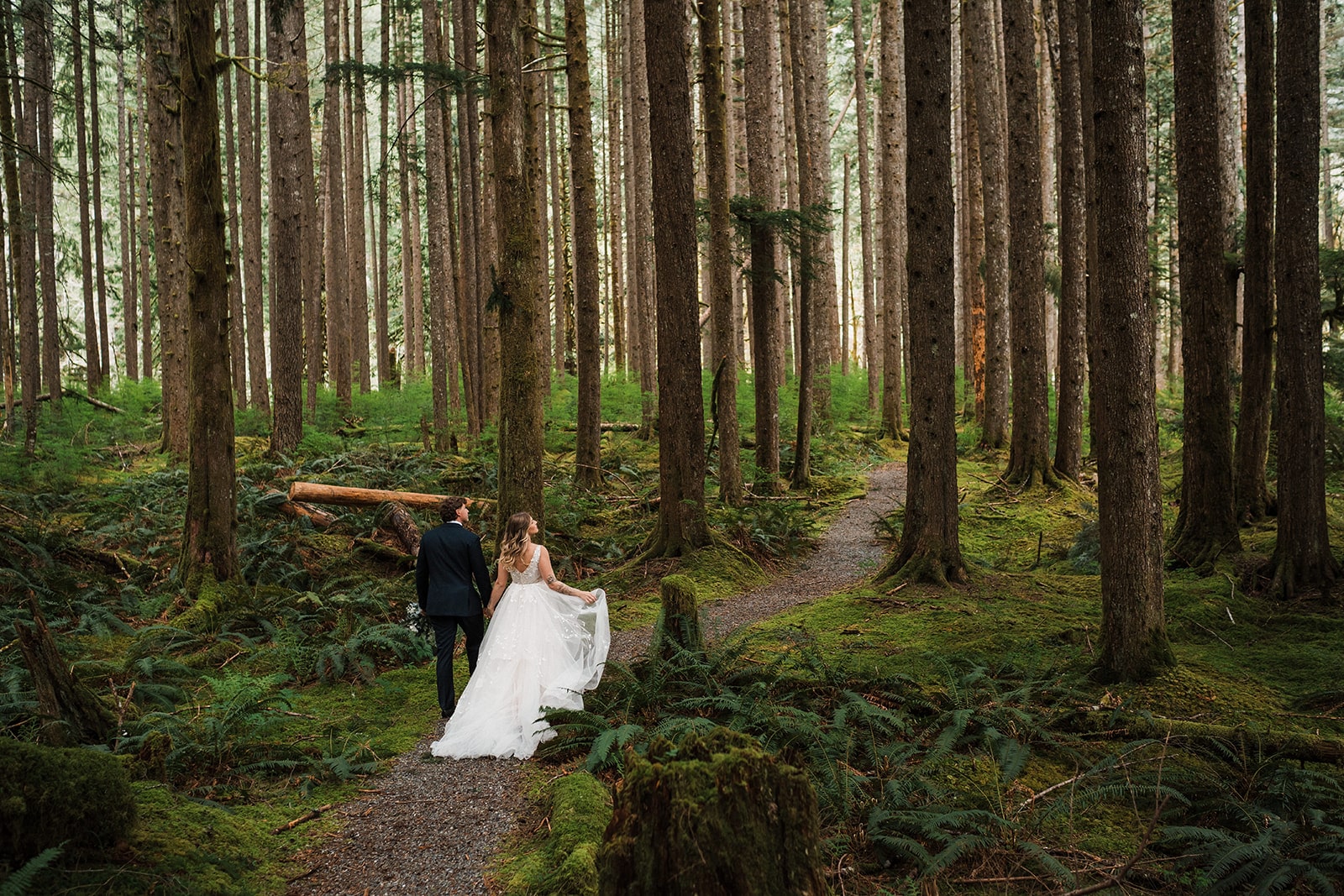 Bride and groom hold hands as they walk through the forest during their elopement with family and friends.