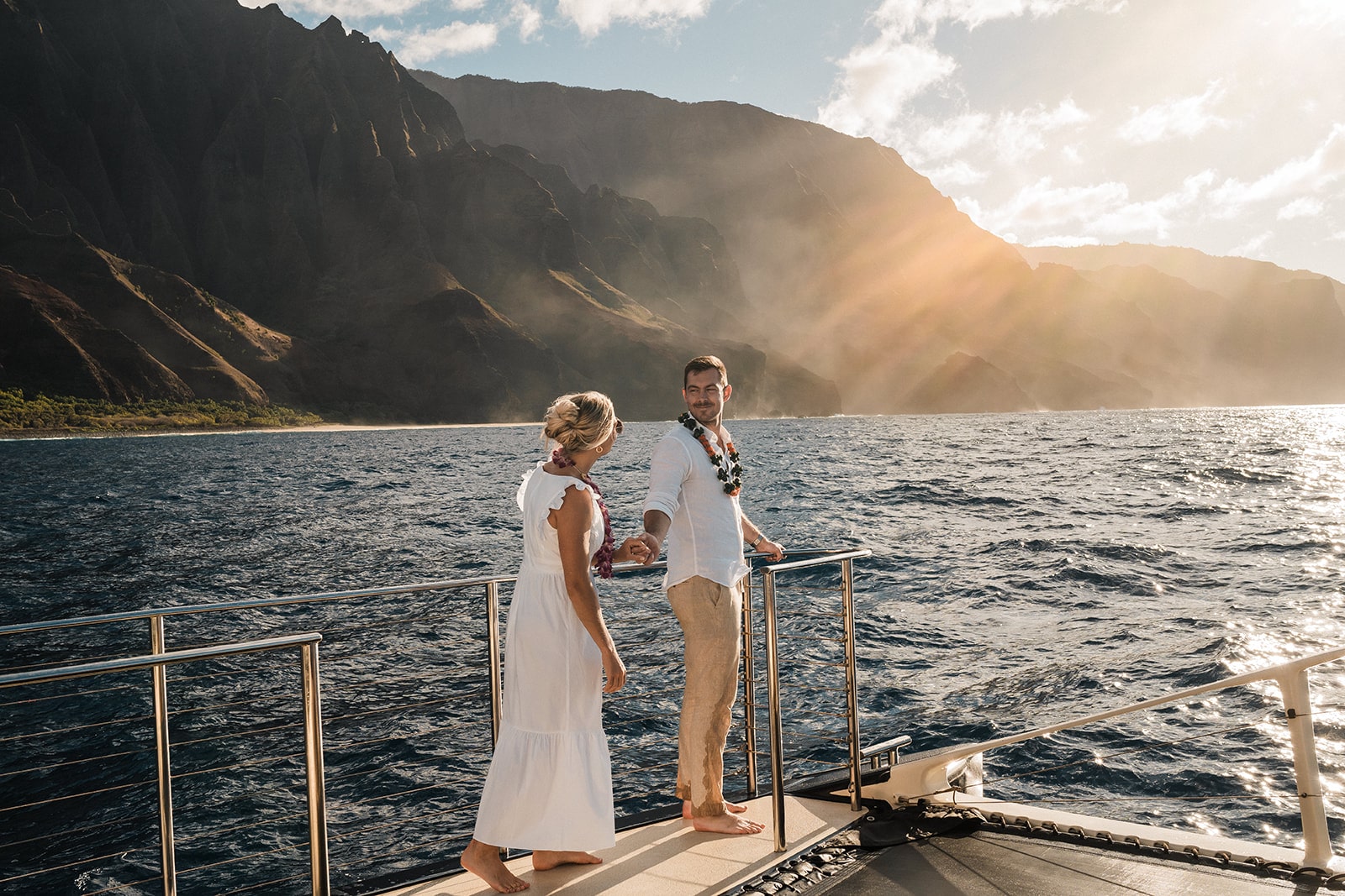 Couple holds hands while walking around the deck of a catamaran boat tour in Kauai.