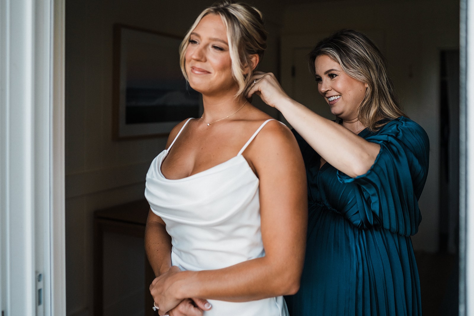 Bride smiles while friend helps her clasp her necklace while getting ready for her Kauai micro wedding.
