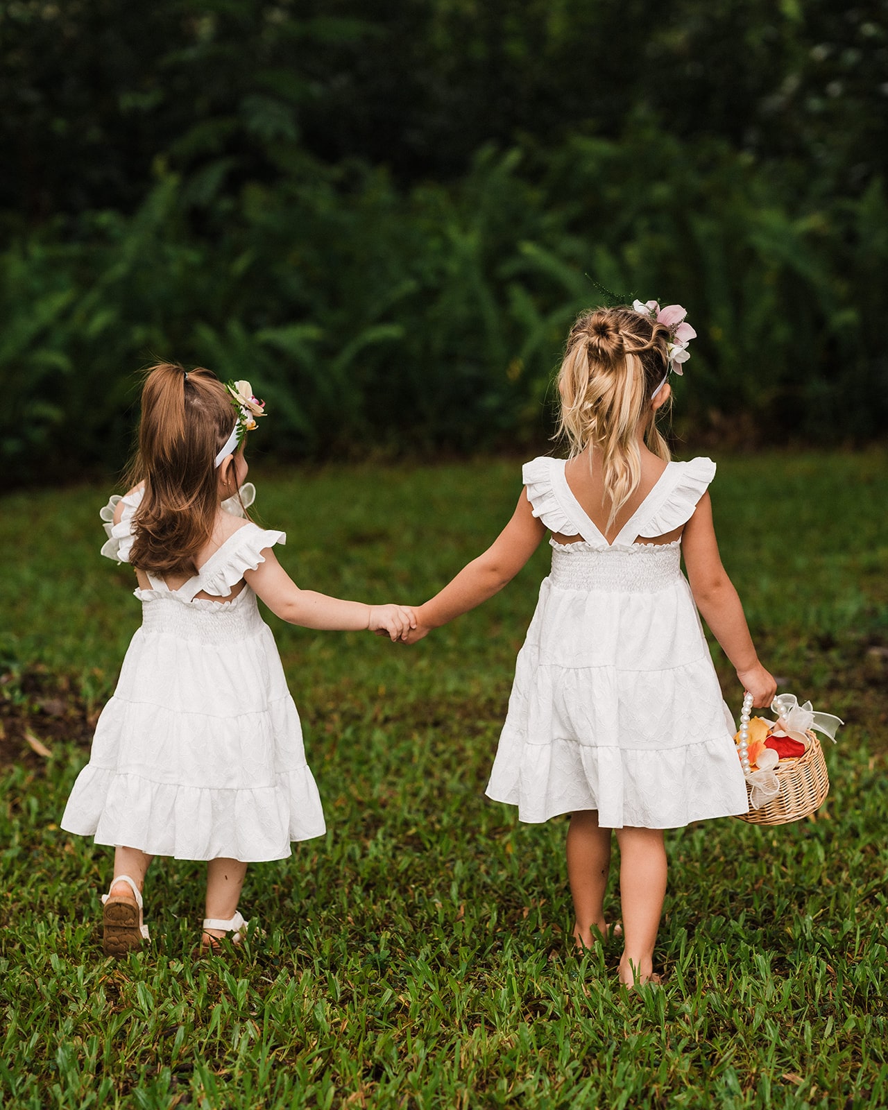Flower girls in white dresses hold hands while walking an aisle of a Kauai micro wedding.