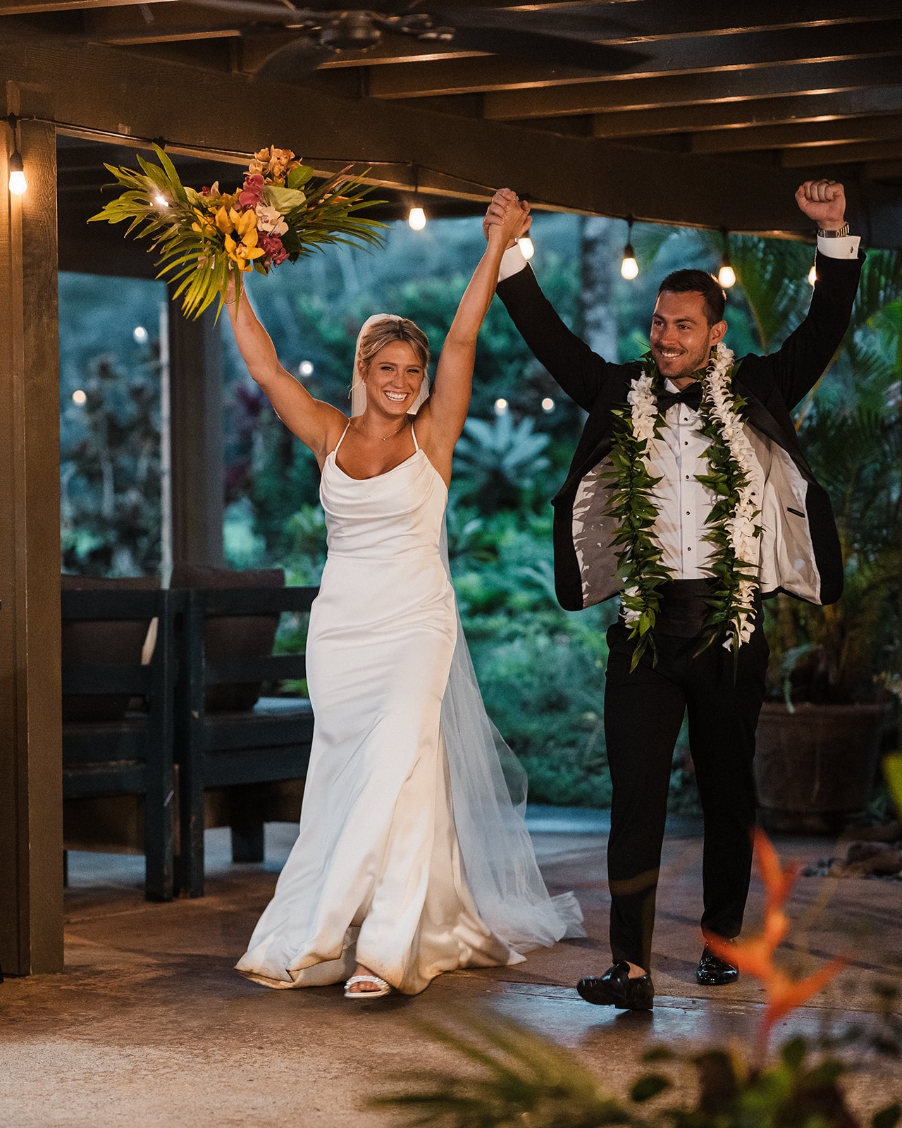 Bride and groom raise their hands in celebration while entering their Kauai micro wedding reception.