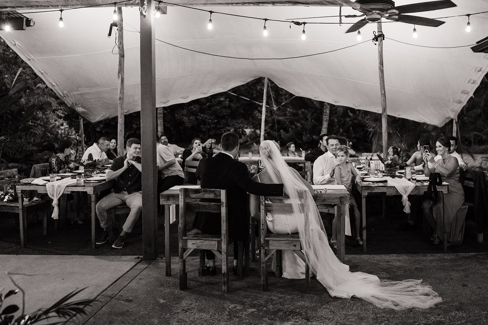 Groom puts arms around bride while sitting at their micro wedding reception dinner in Kauai.