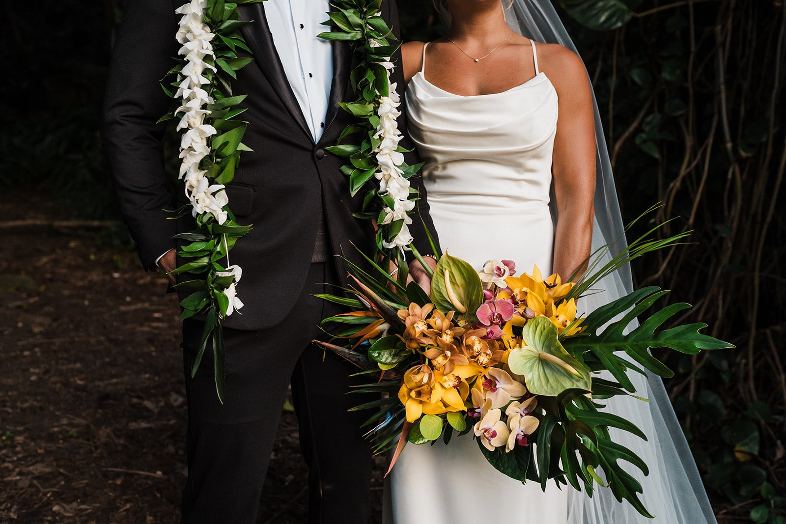 Bride holds a bouquet of tropical flowers while groom wears a white lei at their three-day micro wedding in Kauai.