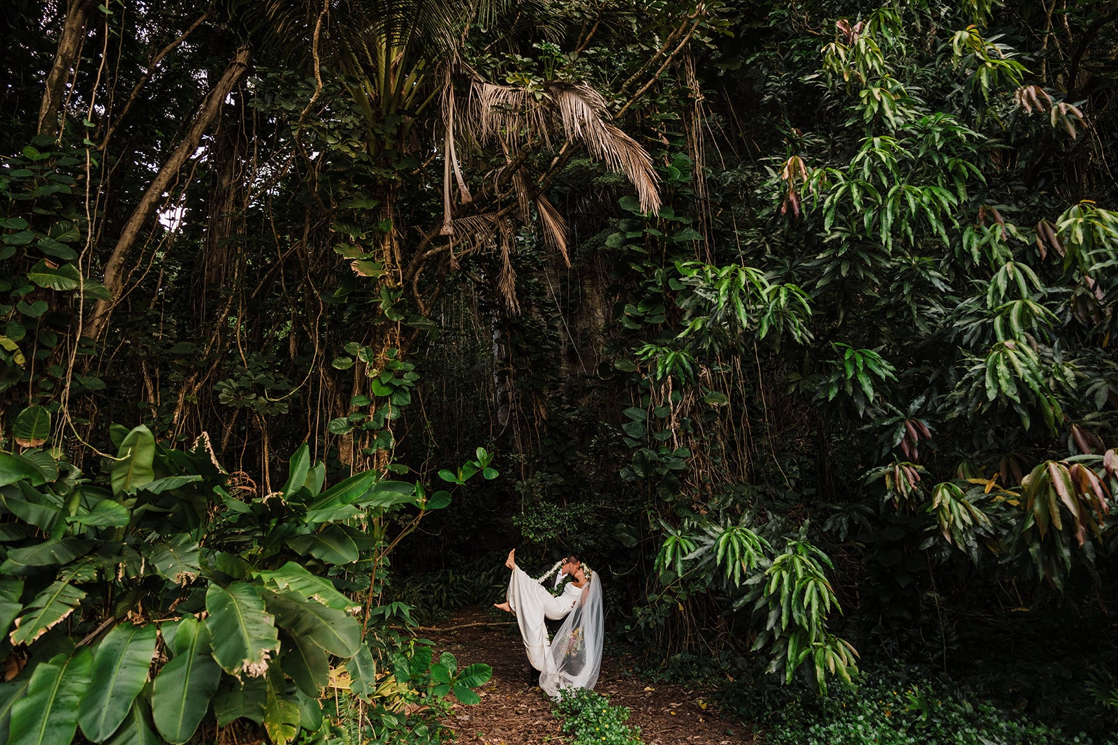 Groom dips bride back for a kiss during their jungle wedding photos in Kauai.