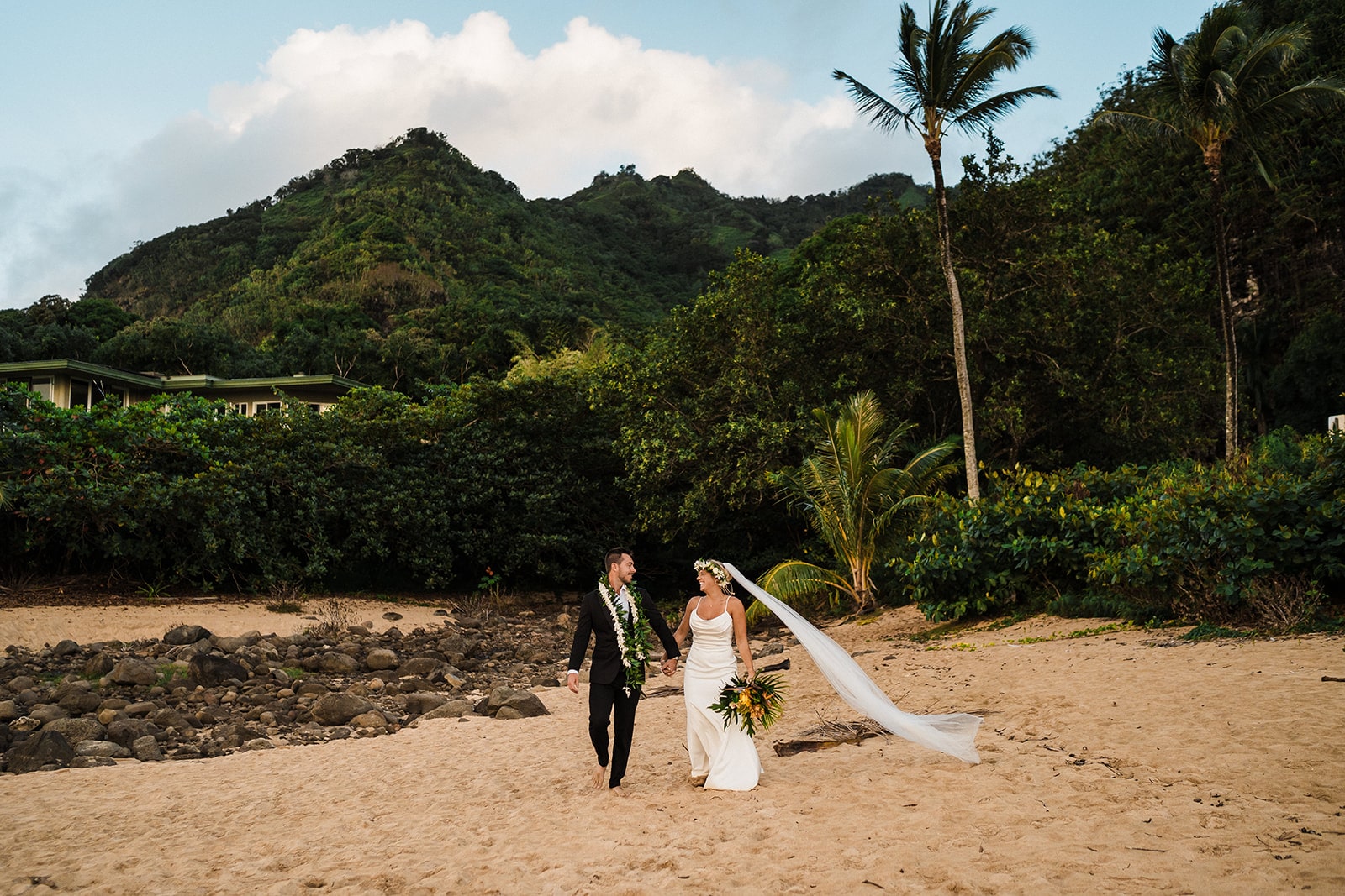 Bride and groom hold hands while walking along the beach during their micro wedding in Kauai.