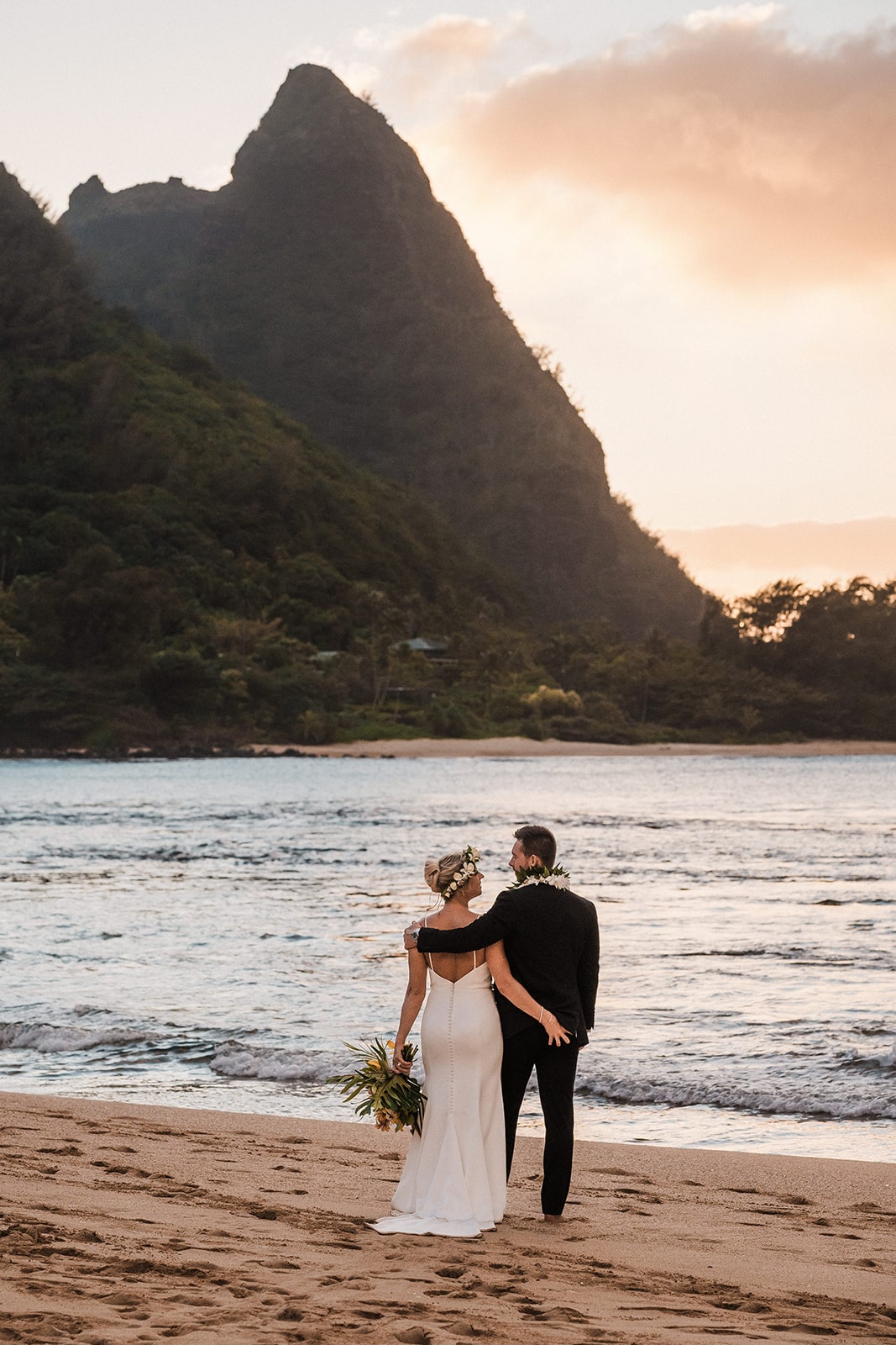 Bride and groom hug side by side on the beach during their Kauai wedding at sunset.