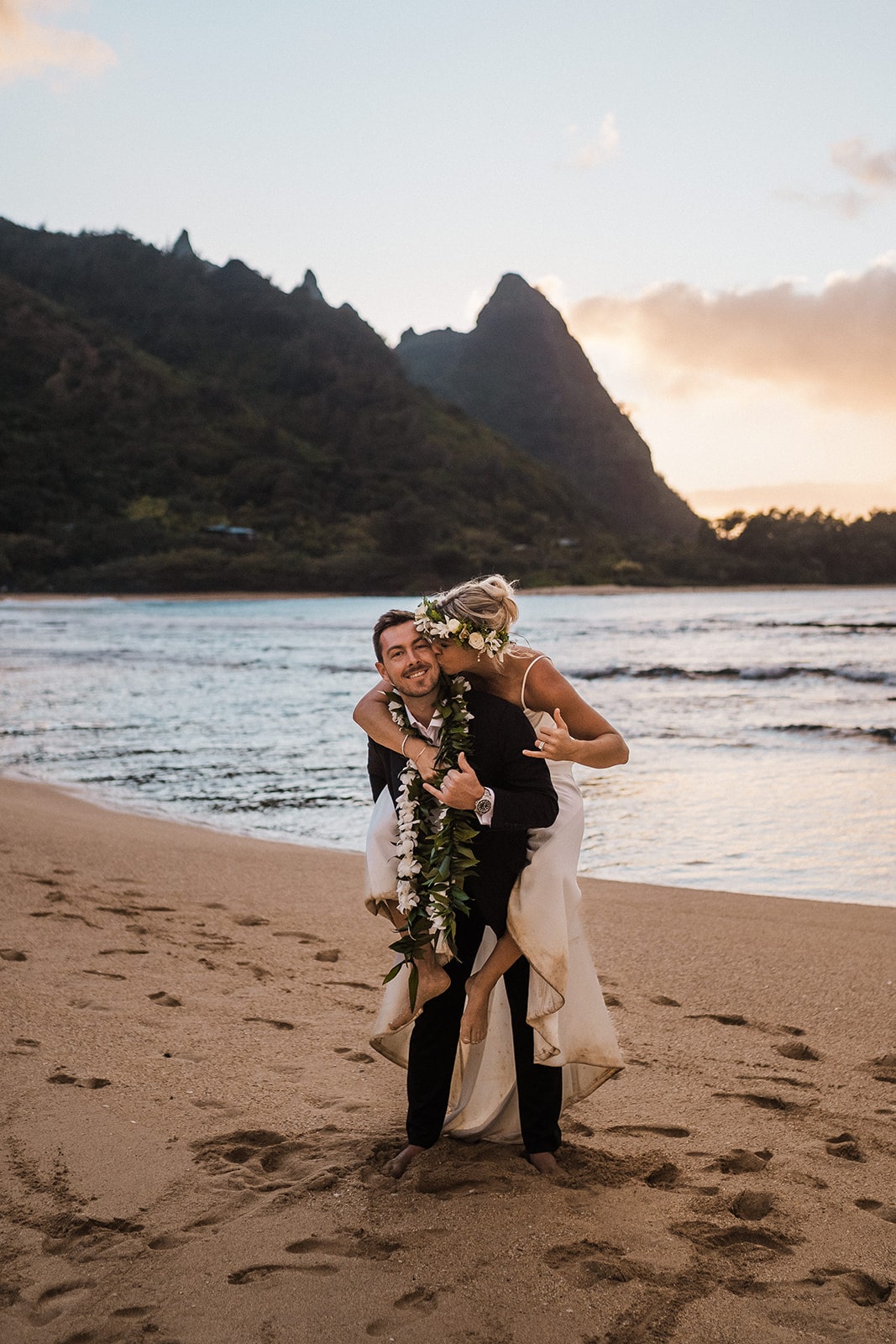 Bride rides on groom's back during their beach wedding in Kauai.