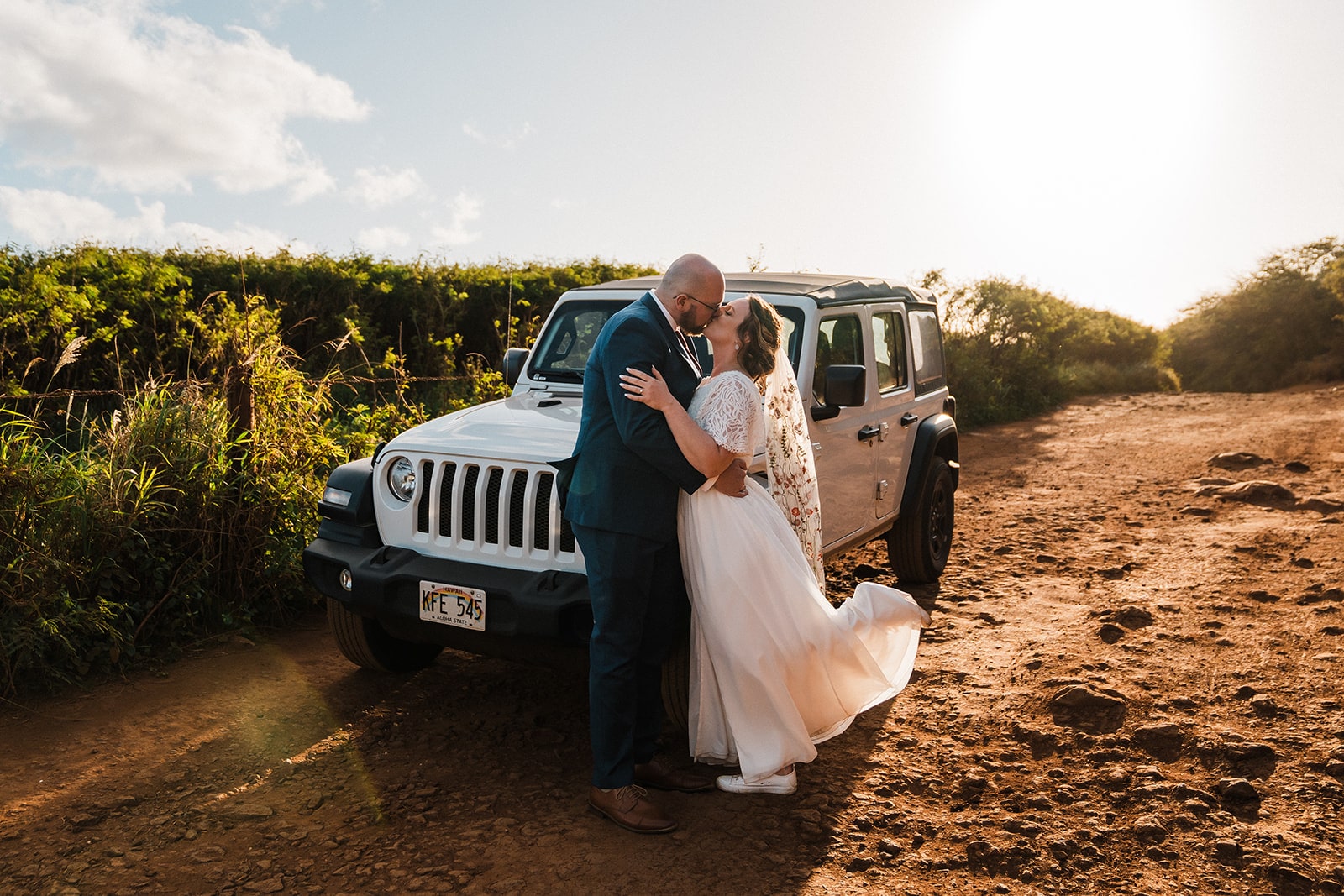 Bride and groom kiss on a red dirt road next to a Jeep during their Kauai Hawaii elopement.