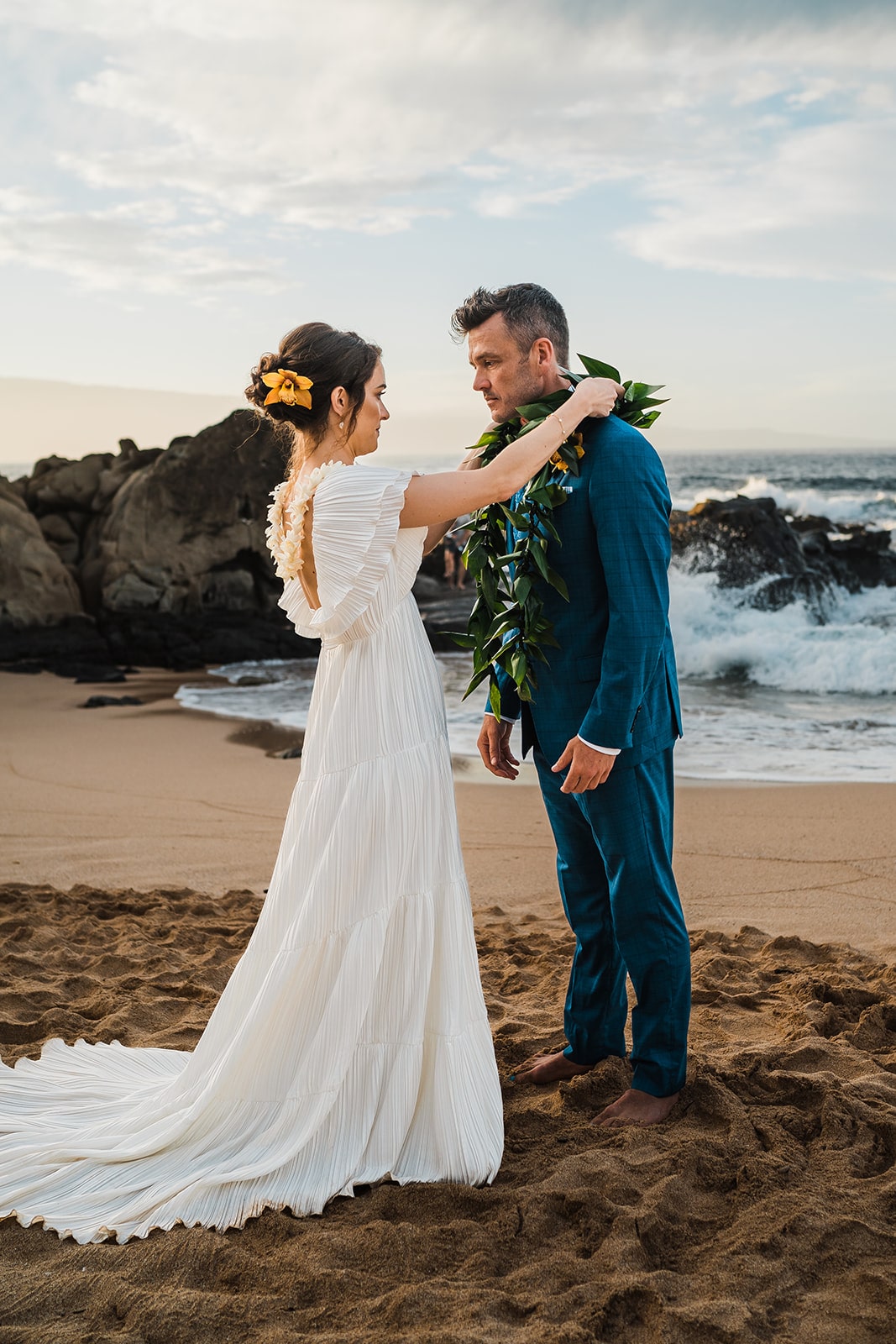 Bride puts a lei around groom's neck during their beach ceremony at their elopement in Kauai.