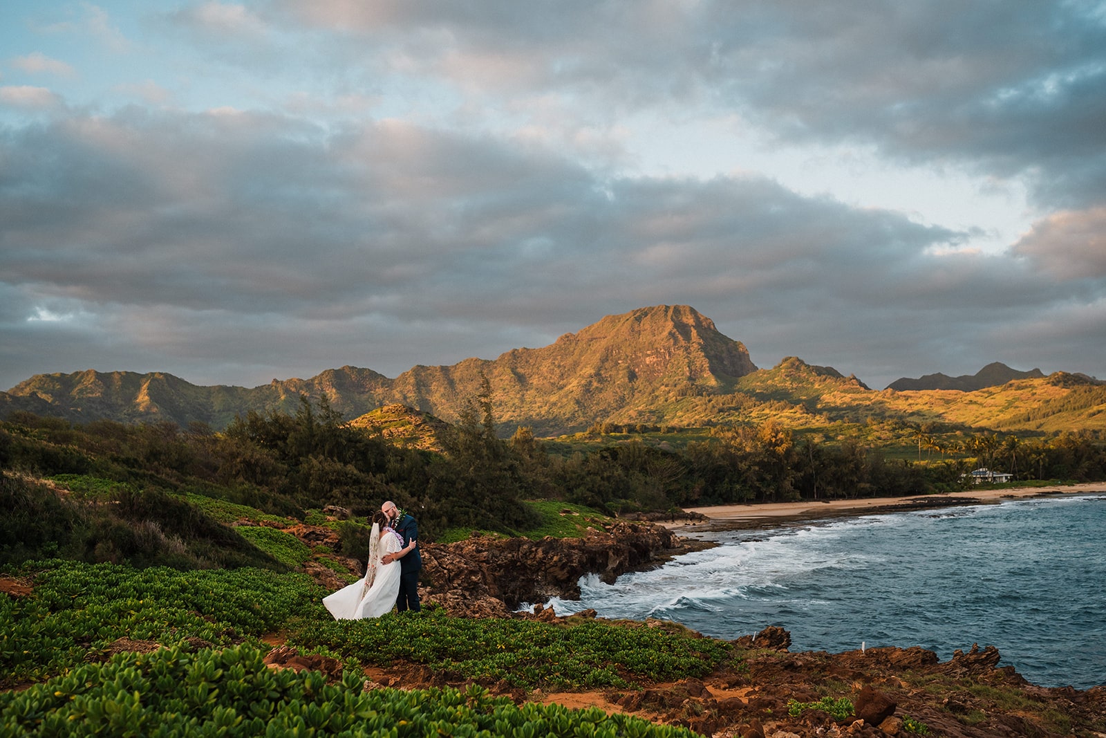Bride and groom kiss on a cliffside at sunset during their elopement in Kauai.