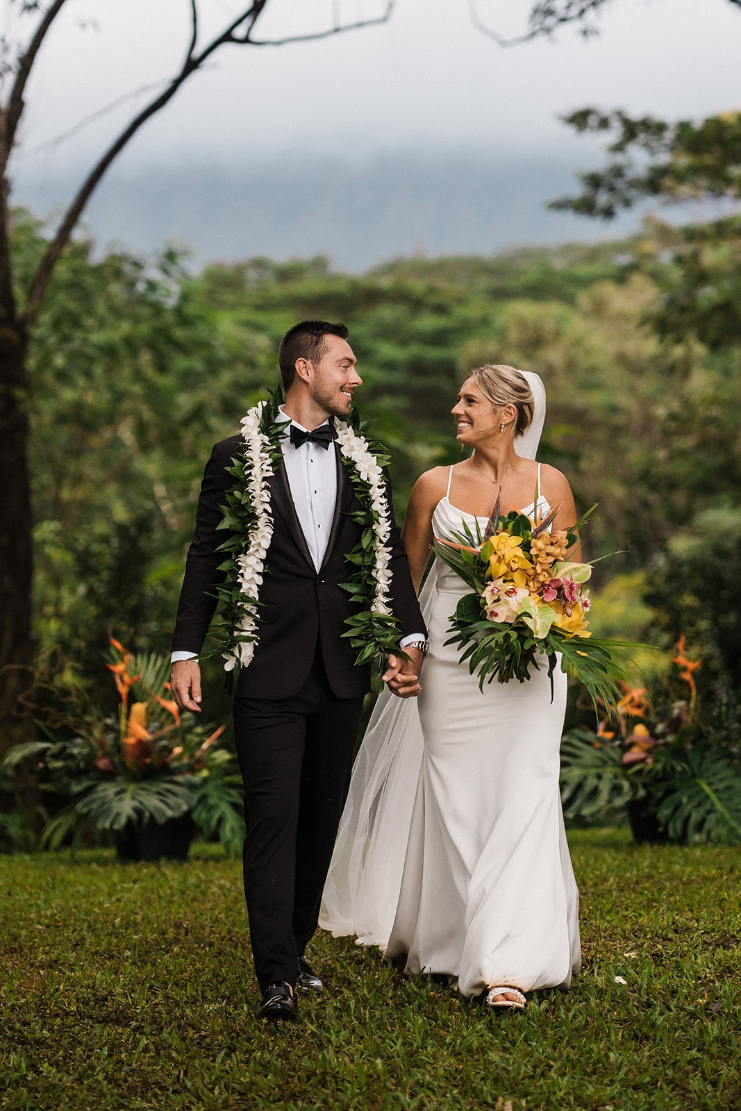 Bride and groom hold hands while walking across the lawn during their small Kauai elopement celebration.
