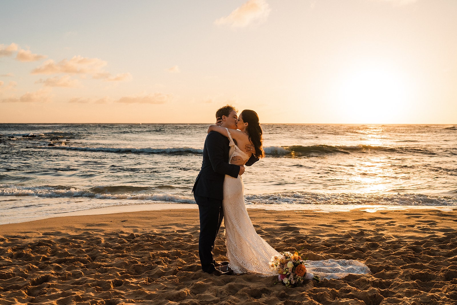 Bride and groom kiss on the beach at sunset while they elope in Kauai.