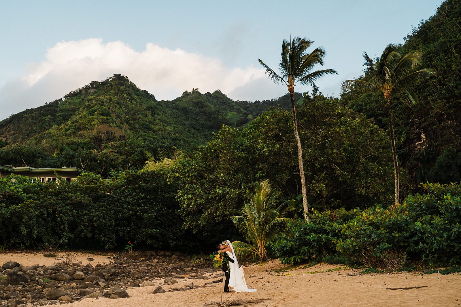 Groom lifts bride for a kiss during their beach elopement in Kauai.