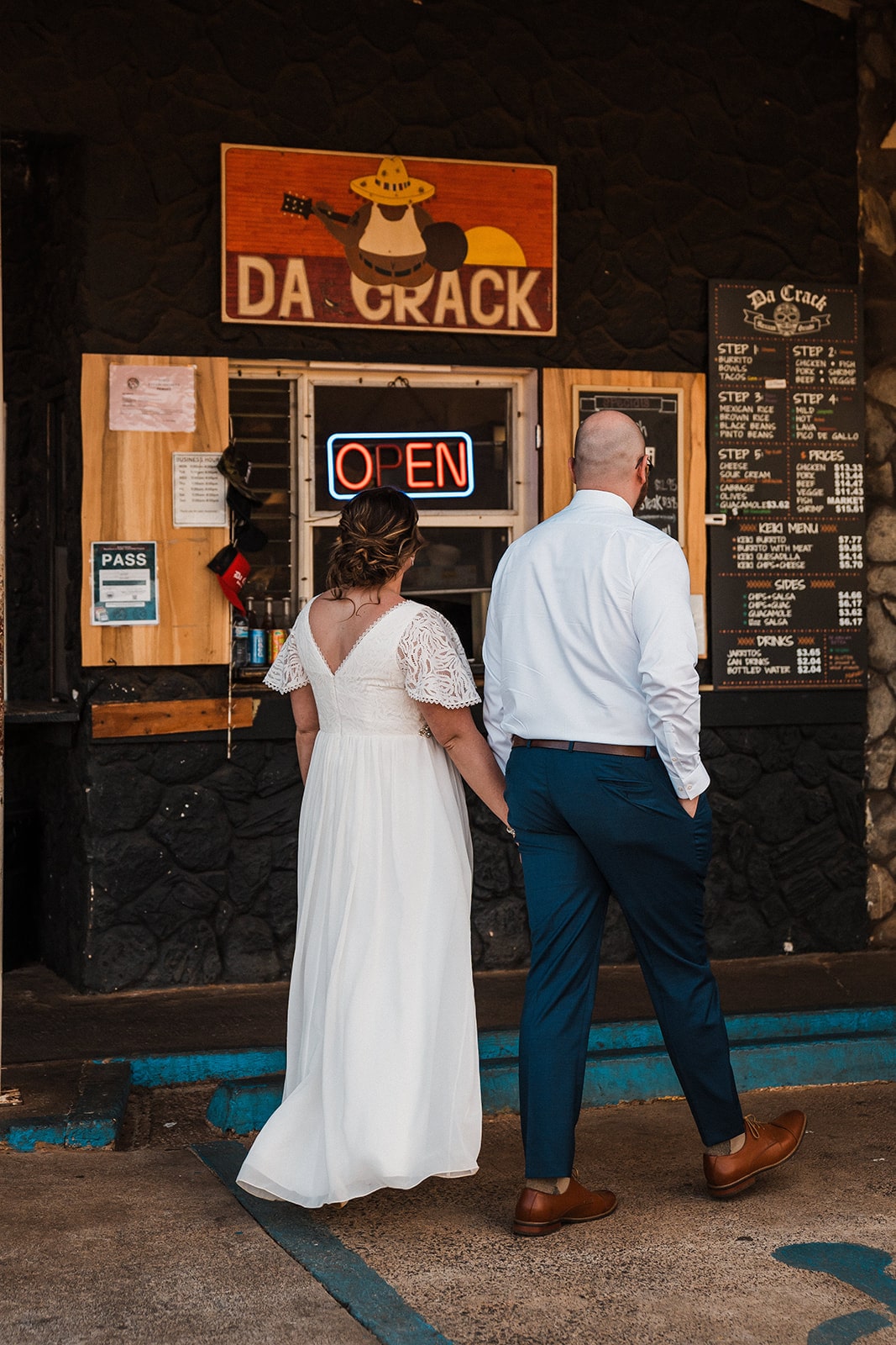 Bride and groom hold hands while they walk up to the counter at Da Crack to order lunch during their elopement in Kauai.
