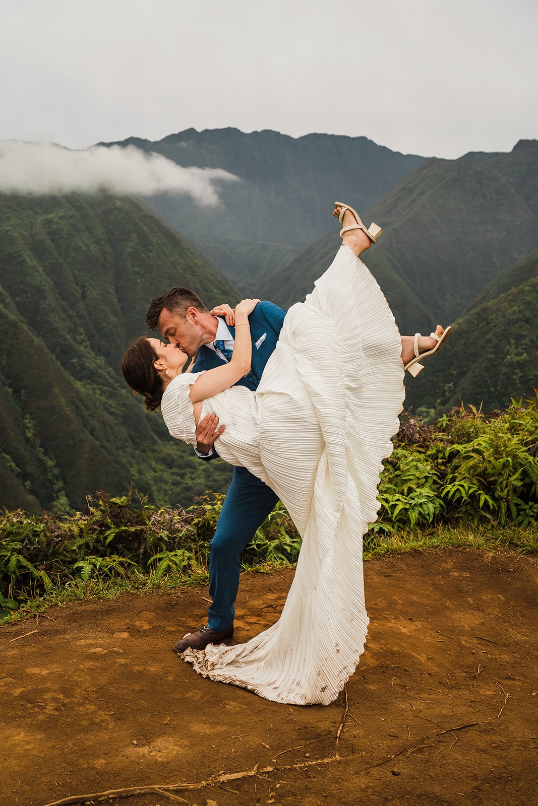 Groom dips bride back for a kiss during their adventure elopement in Kauai at Waimea Canyon.