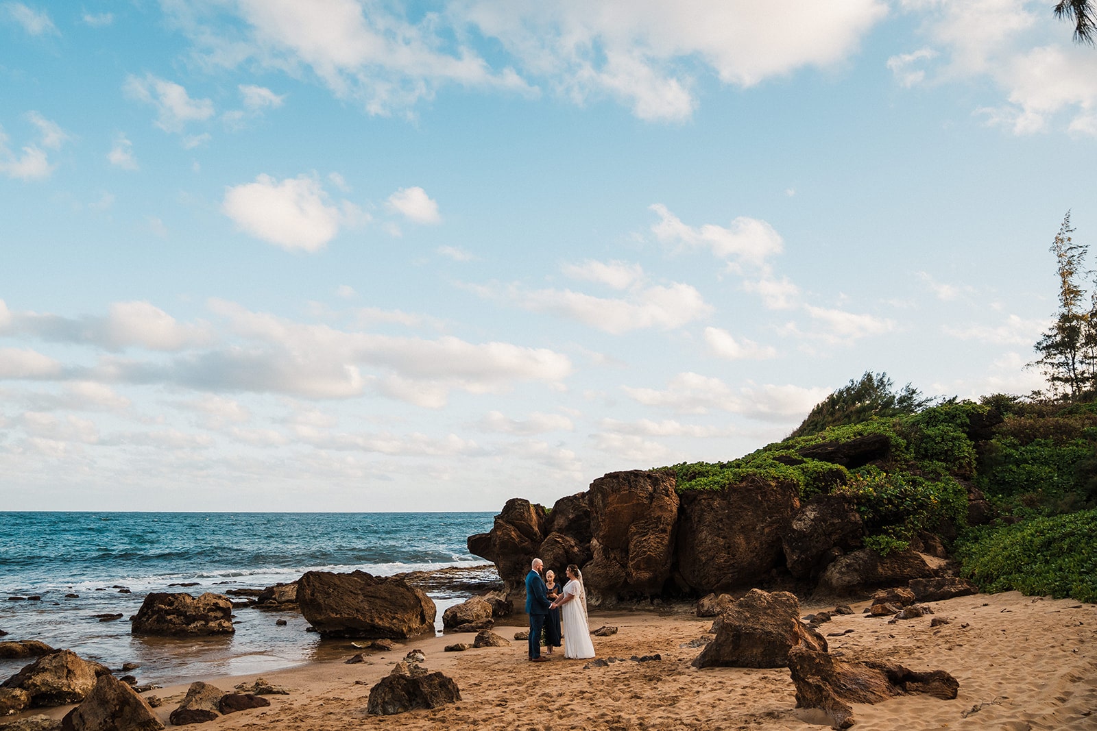Bride and groom hold hands on a beach during their Kauai elopement ceremony with an officiant.