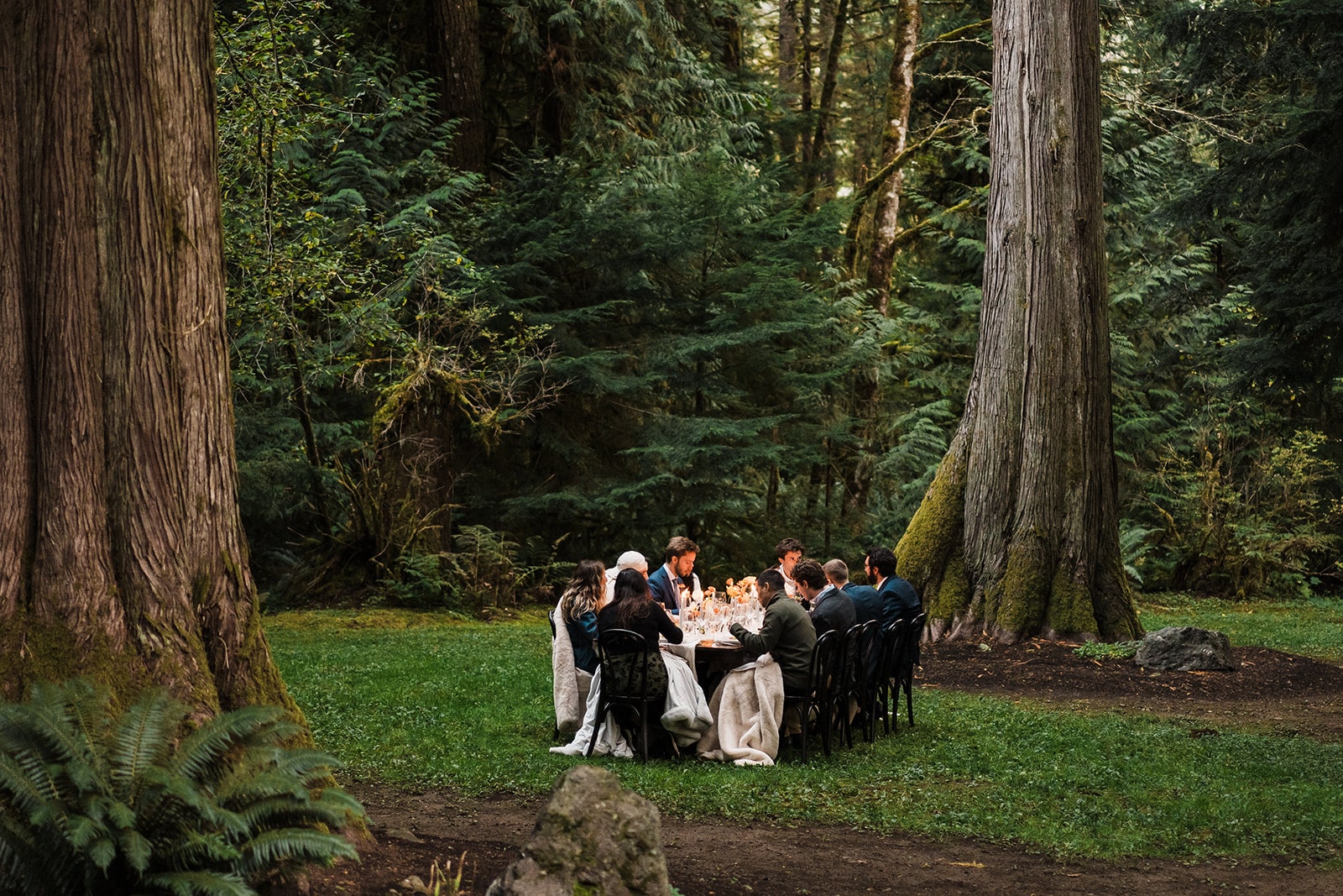 Bride and groom enjoy a candlelit dinner reception in the forest with their guest at their multi-day wedding.