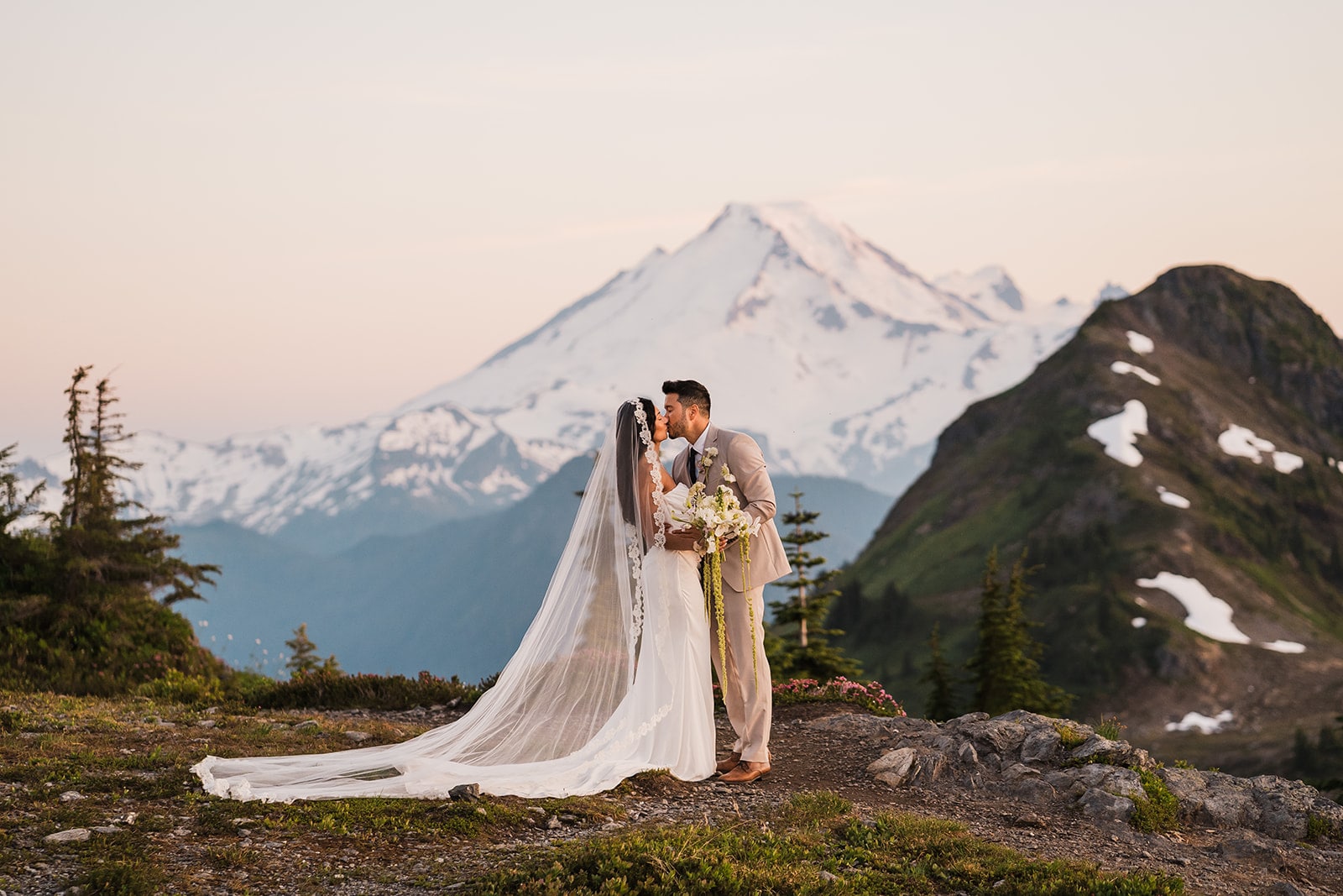 Bride and groom kiss on a mountain trail at sunset during their elopement in the North Cascades.
