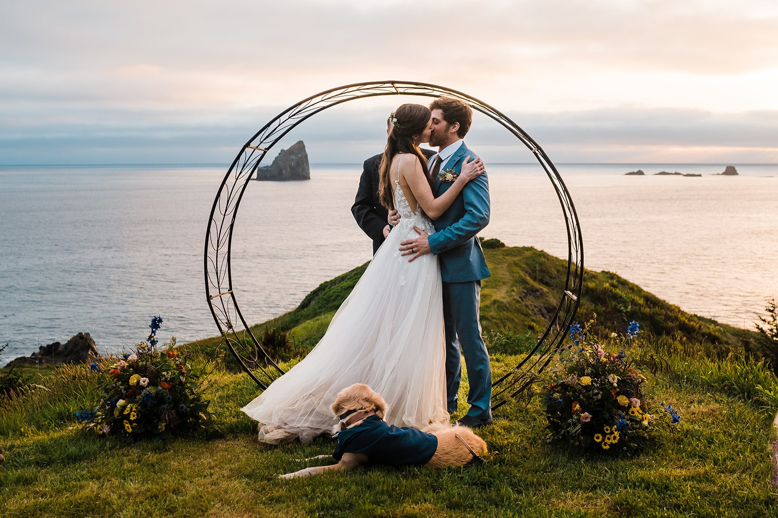 Bride and groom kiss at their Oregon Coast elopement while their golden retriever dog lays at their feet.