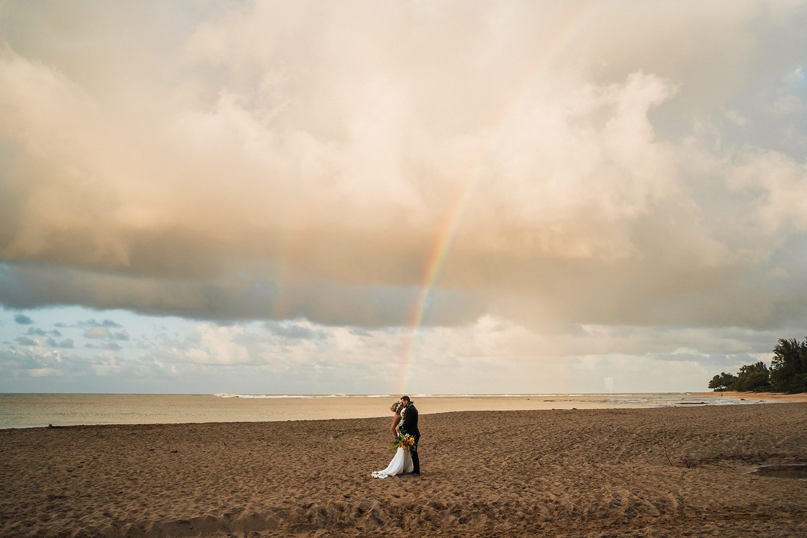 Bride and groom kiss on a beach at sunset at one of the best Kauai elopement locations on the island.